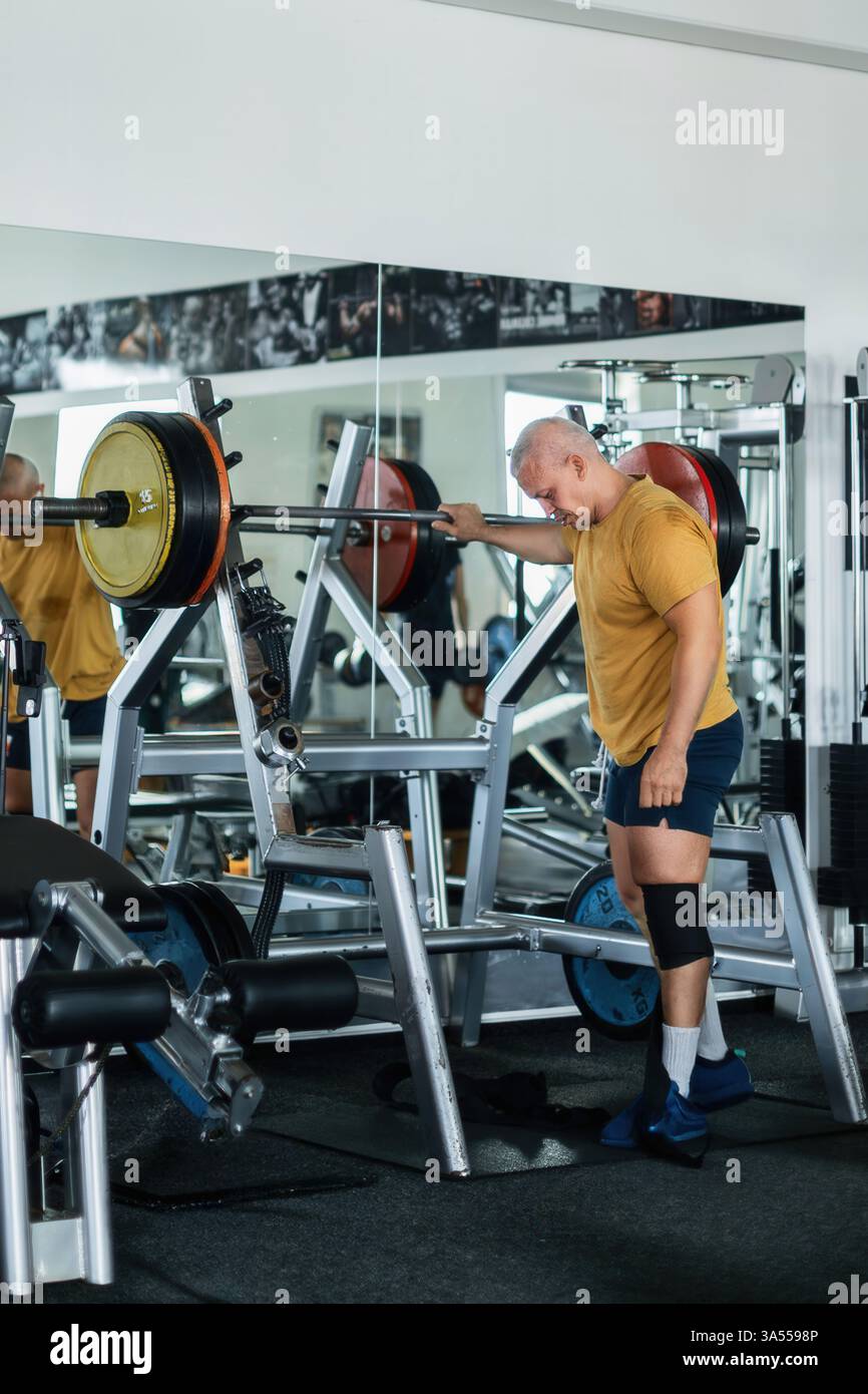 Uomo muscoloso che riposa dopo una sessione di squat impegnativa in palestra Foto Stock