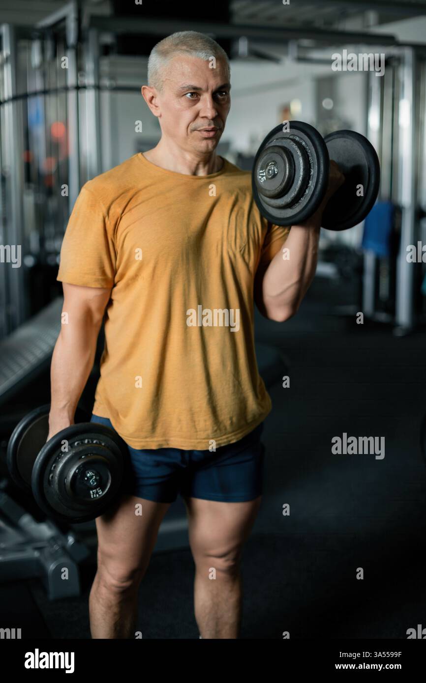 Uomo concentrato che solleva manubri durante un allenamento di forza in palestra Foto Stock