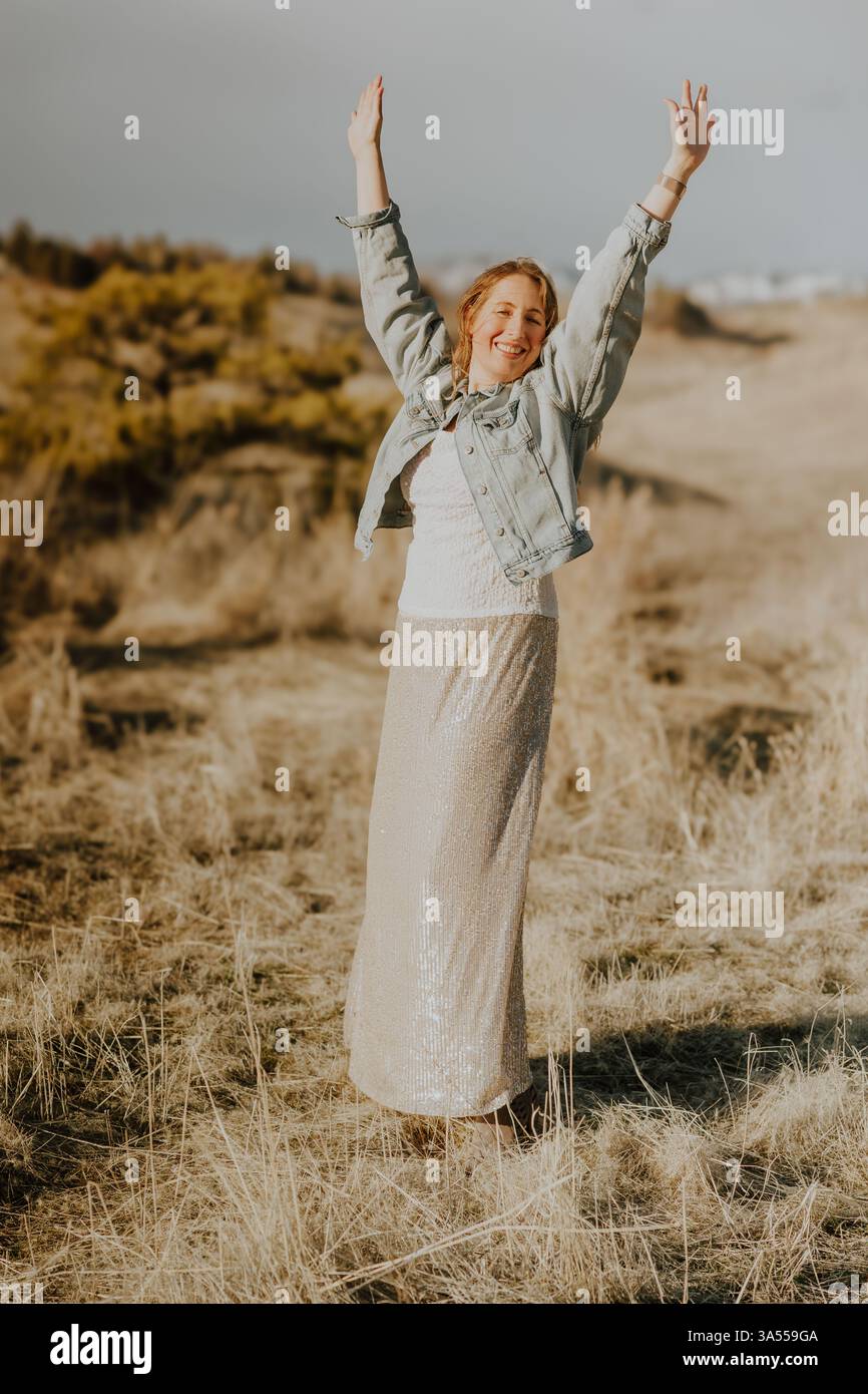 Una donna alza le braccia di gioia, mentre si diffonde in un campo d'oro Foto Stock