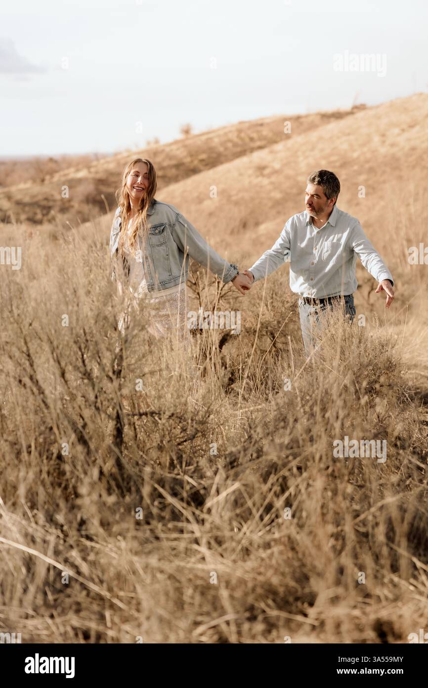 Un paio cammina mano nella mano, esplorando insieme una collina illuminata dal sole Foto Stock