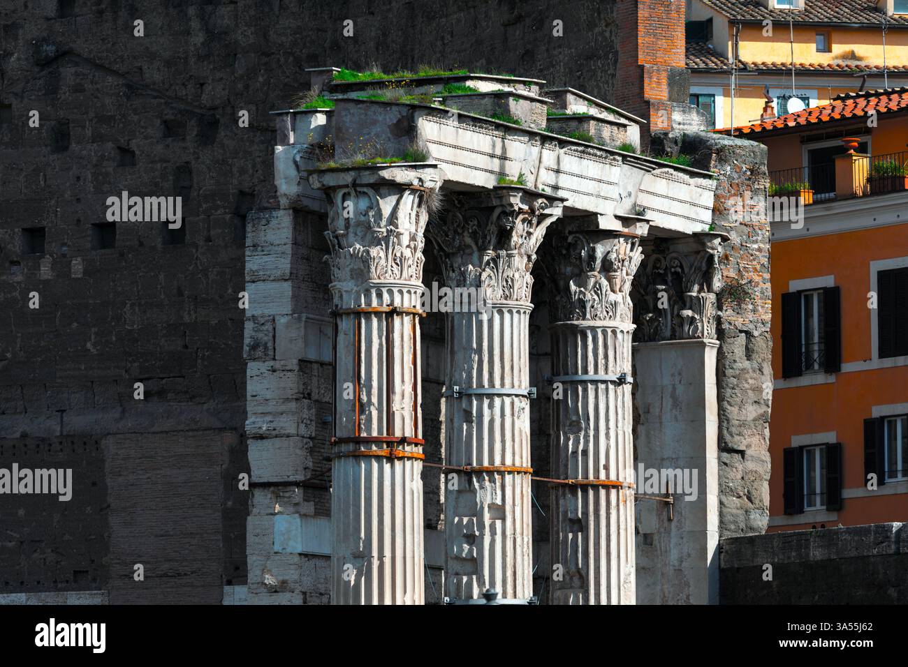 Le antiche colonne corinzie del tempio romano sono conservate contro pareti in mattoni, con edifici moderni sullo sfondo. Rinforzi in metallo arrugginito Foto Stock