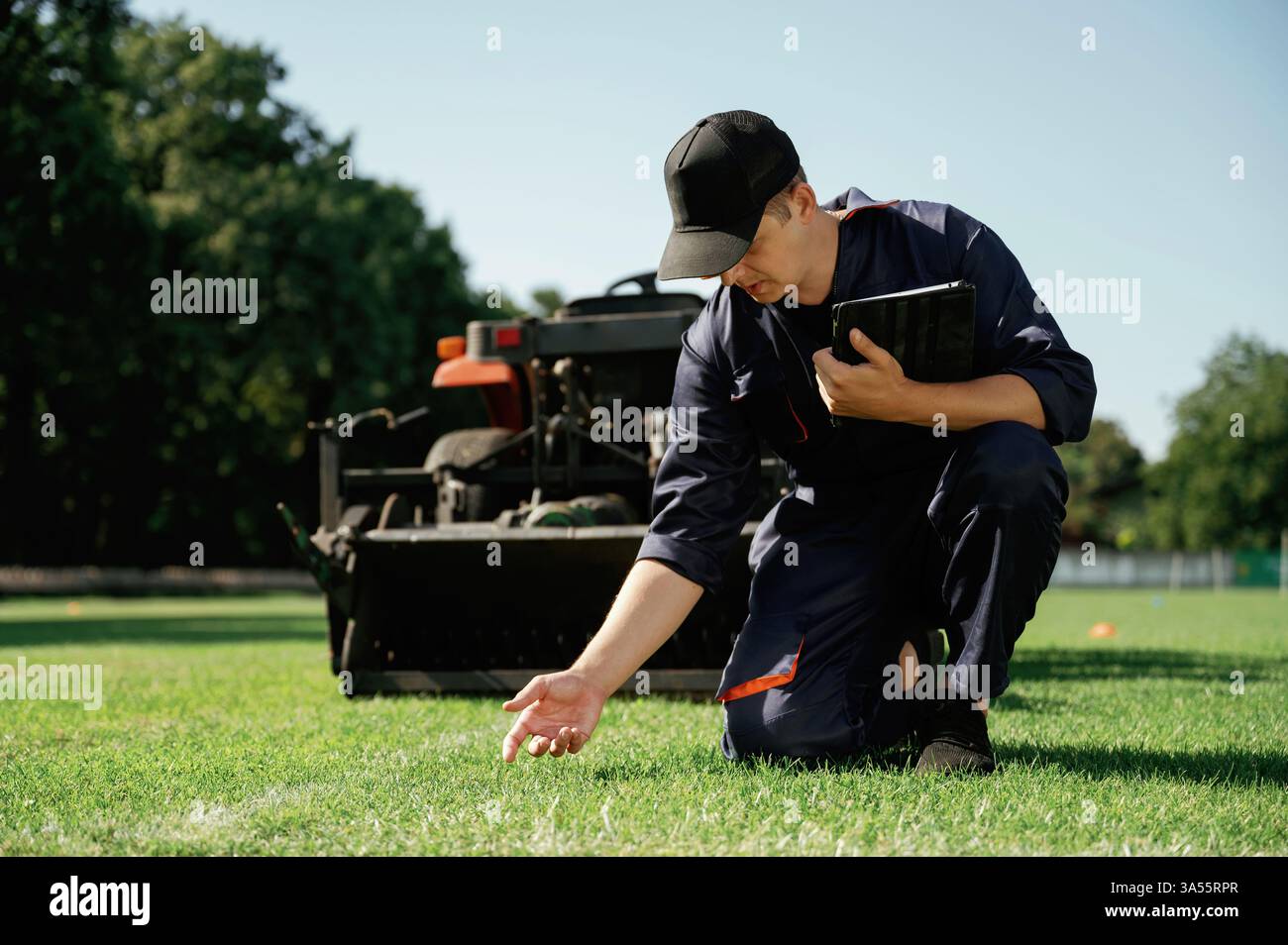 Controllo qualità, contatto con l'erba. Man è con un trattore multiuso con attrezzature per aeratori e tagliaerba sul campo. Foto Stock