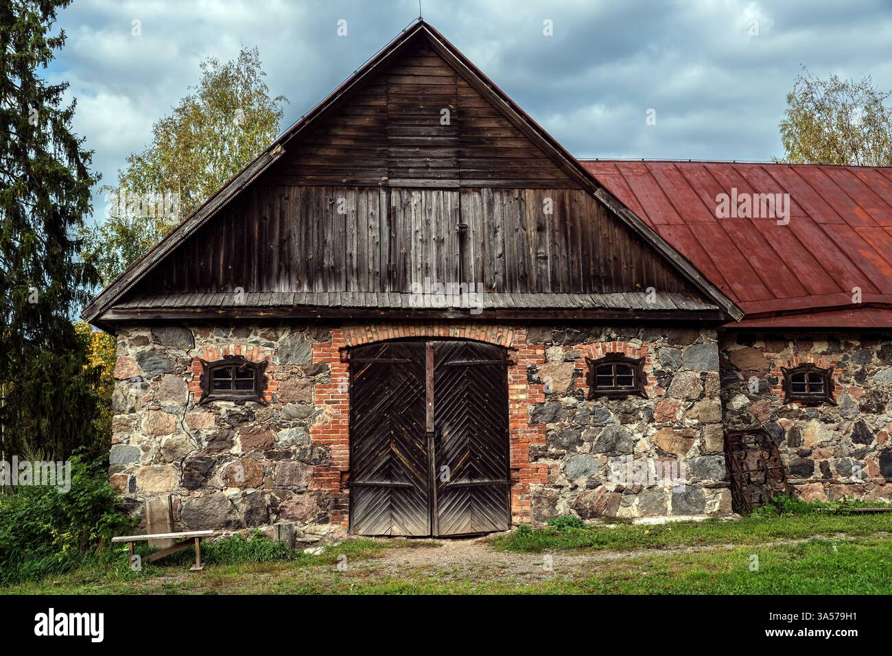 Vecchio fienile costruito in pietra e mattoni, con grandi porte in legno e piccole finestre. Foto Stock