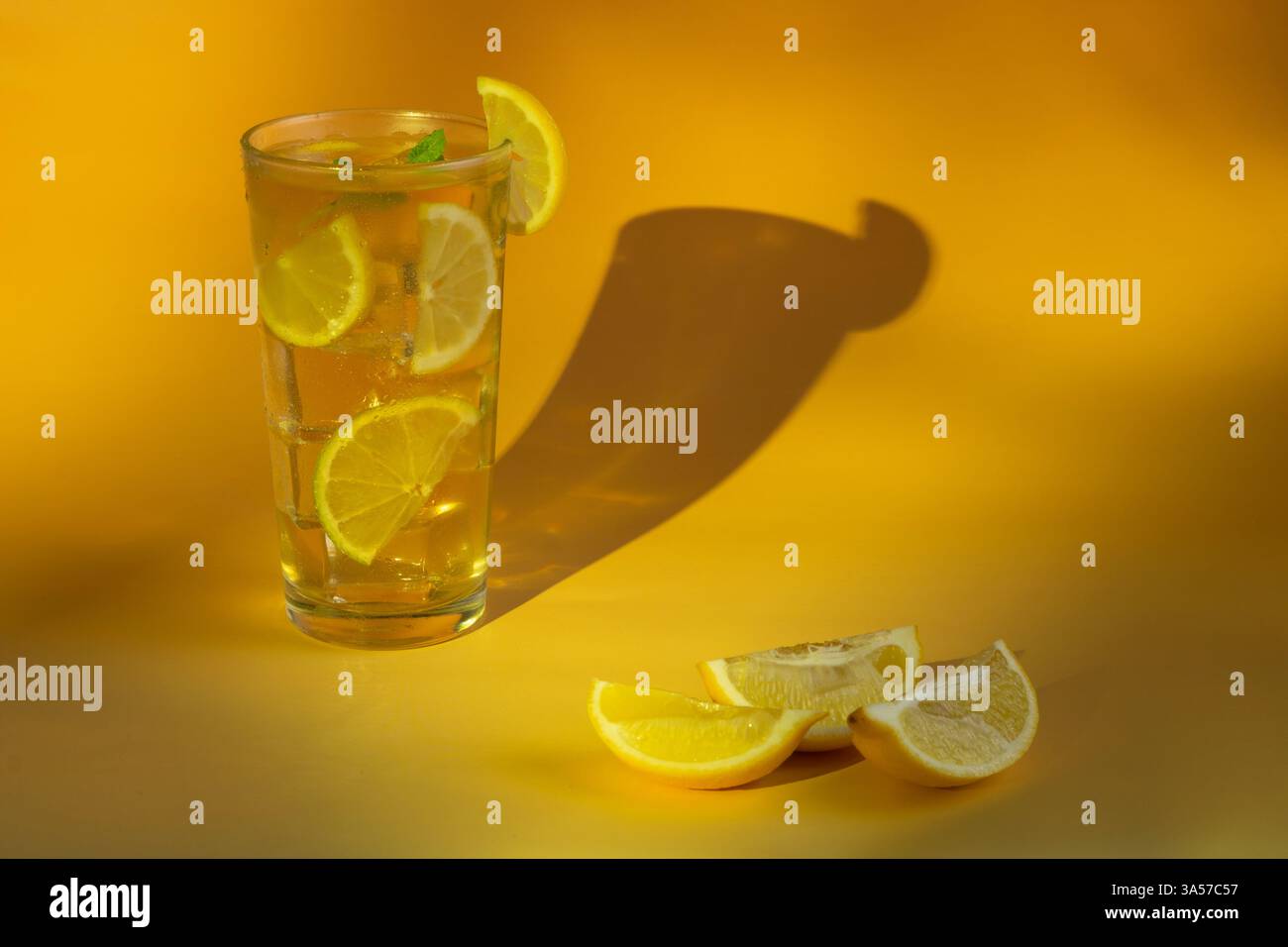 Un bicchiere di tè ghiacciato con fette di lime e limone. La bevanda è servita in un bicchiere con foglie di menta sulla parte superiore. Tre spicchi di limone sul lato. Foto Stock