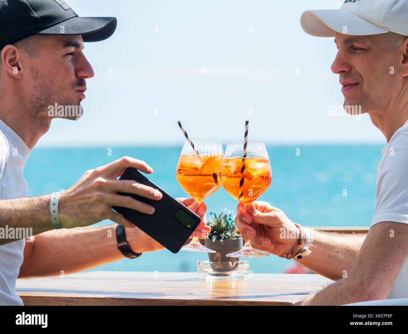 Fuengirola, Malaga, Spagna .03/15/2025. Coppia gay che brinda con un cocktail sul lungomare Foto Stock