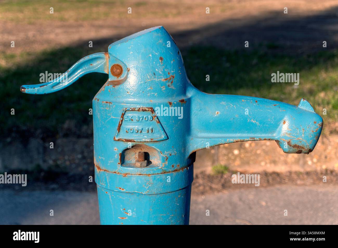 La pompa d'acqua ungherese d'epoca è esposta in modo prominente in un parco soleggiato, circondato da erba verde. La superficie metallica mostra segni di ruggine, che si aggiunge Foto Stock