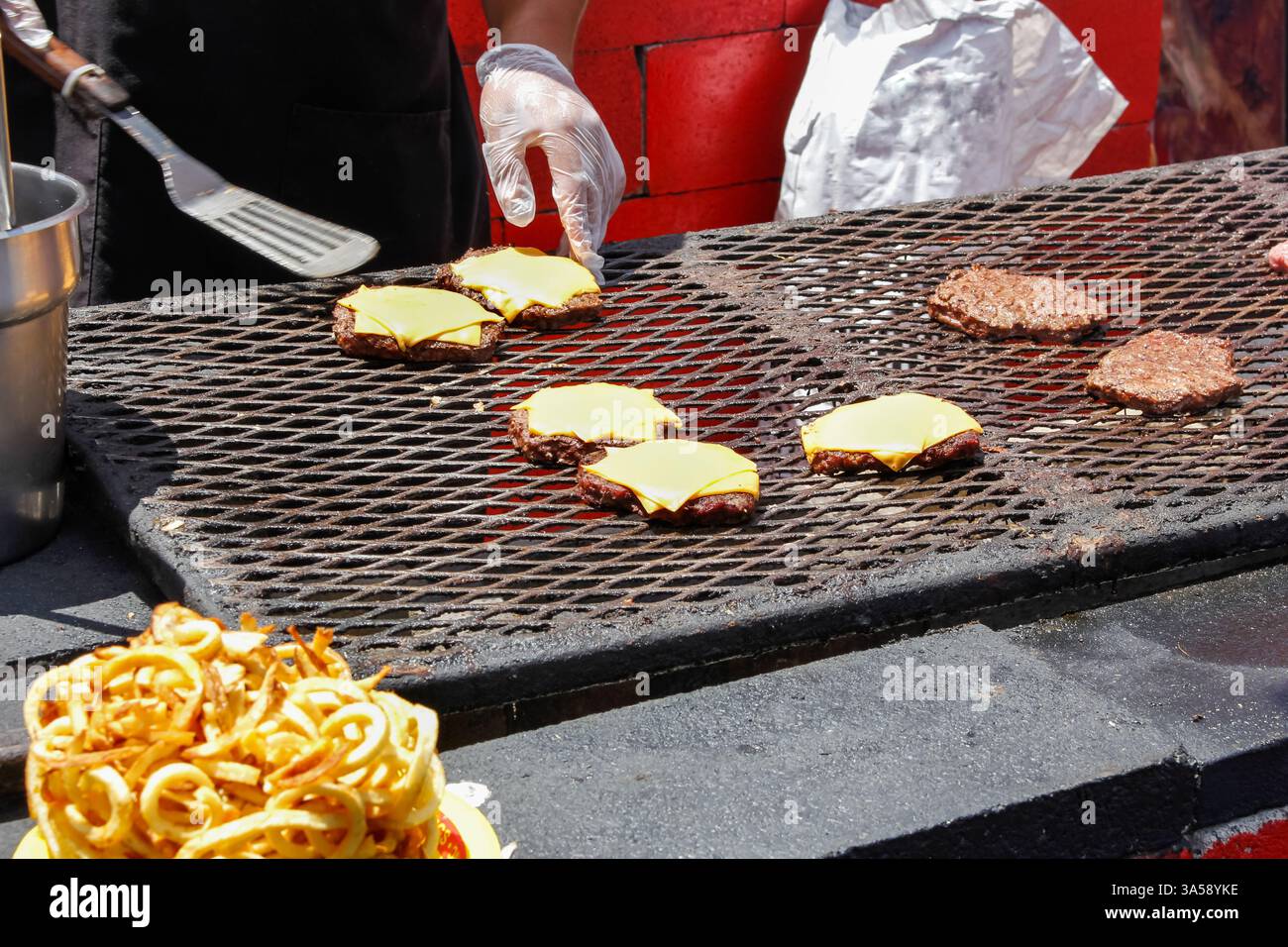 Vista delle mani di un cuoco che prepara hamburger con formaggio su una grande griglia. Foto Stock