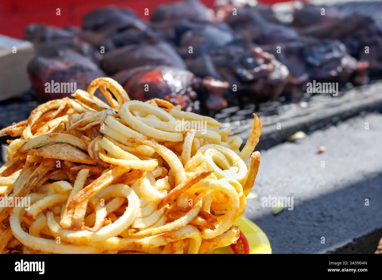 Una vista ravvicinata di un grande mucchio di patatine fritte, davanti a diverse grandi zampe di tacchino, su un barbecue commerciale. Foto Stock