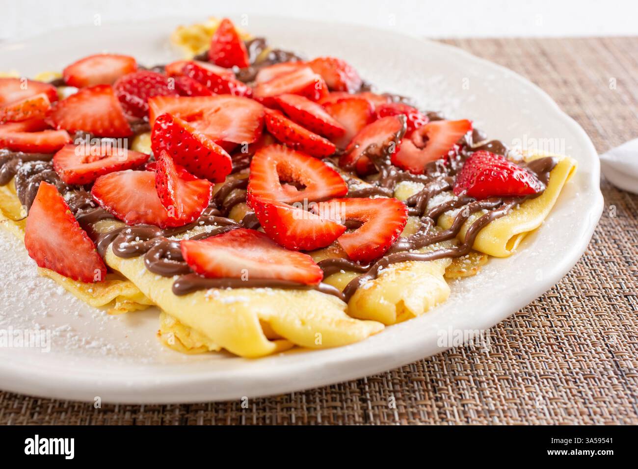 Una vista delle crepe su un piatto, ricoperte di crema di cioccolato alle nocciole e fette di fragola. Foto Stock