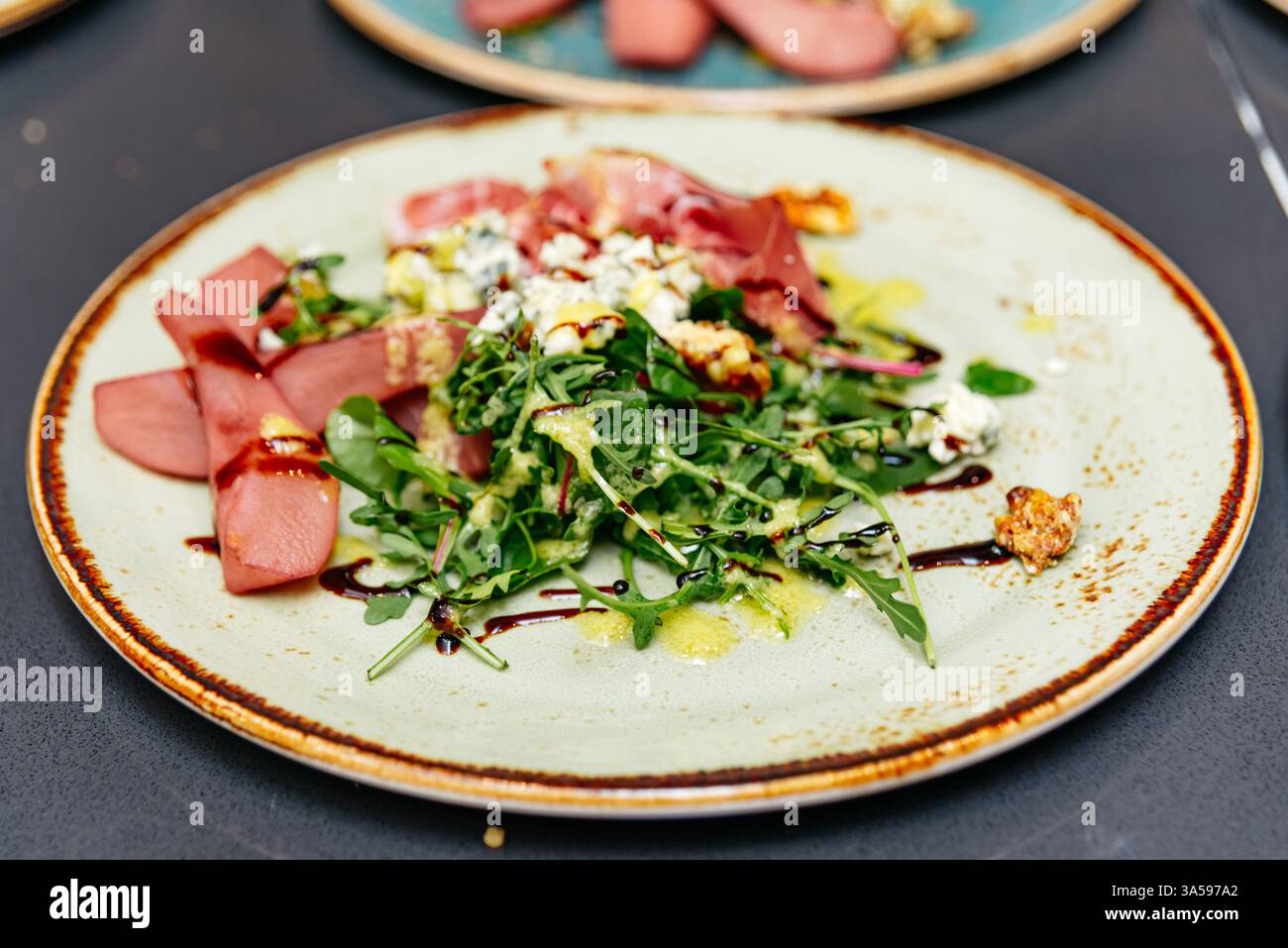 Insalata gourmet di rucola con pere in camicia, prosciutto, formaggio blu, noci candite e glassa balsamica, elegantemente decorata per cene raffinate. Foto Stock