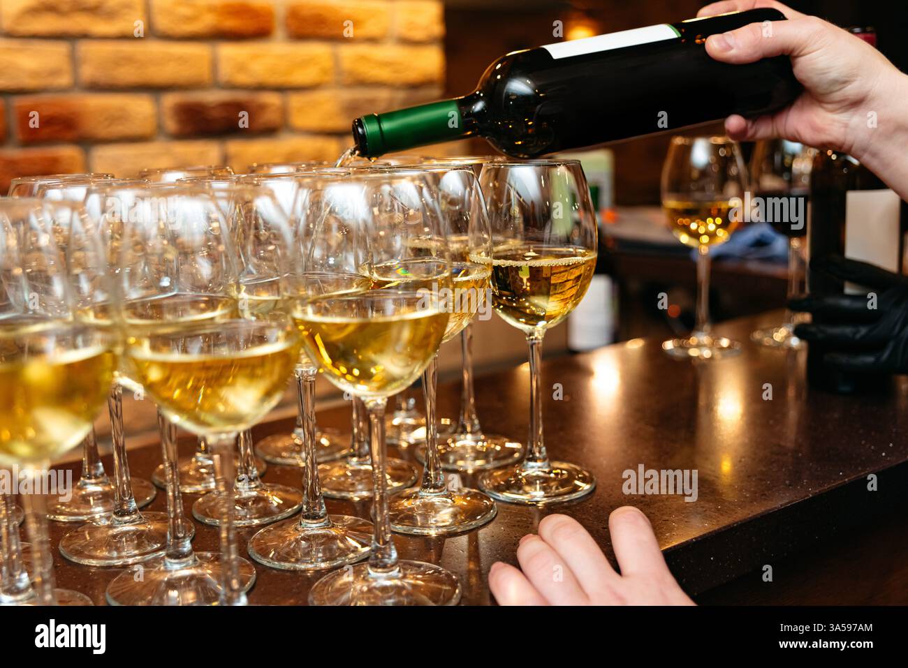 Un barista versa vino bianco in più bicchieri presso un bar, preparandosi per un evento elegante o un'esperienza di degustazione di vini. Foto Stock