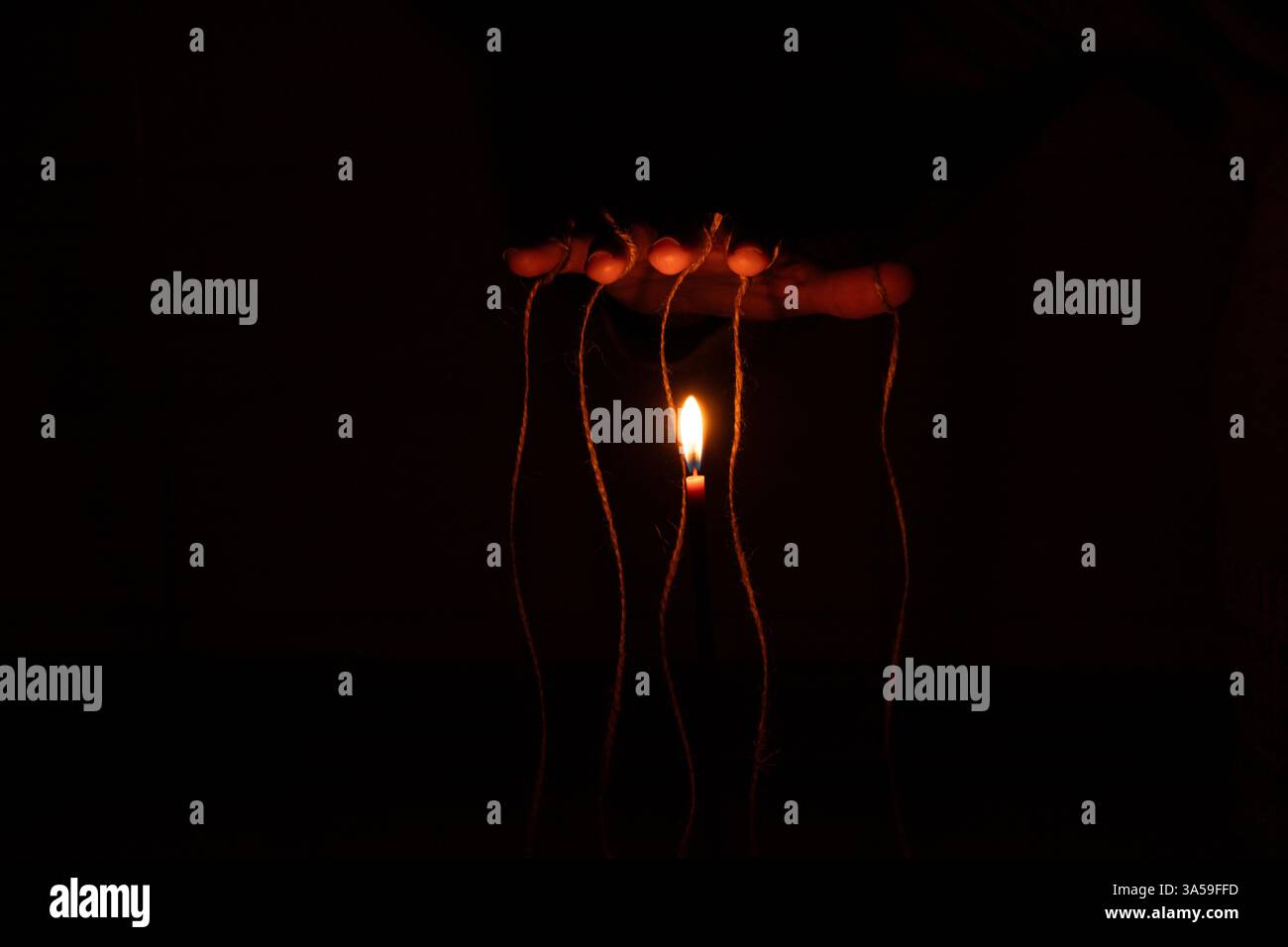 Mano femminile con corde sulle dita al buio vicino a candela, burattinaio, controllo sulle persone, forza le mani Foto Stock
