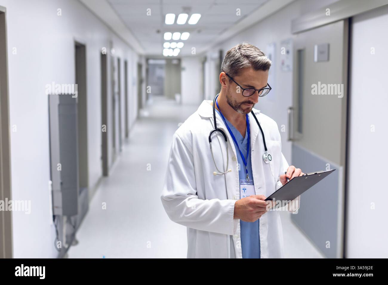 Medico nei corridoi dell'ospedale che rivede la cartella paziente, si concentra sulle attività sanitarie, copia spazio Foto Stock