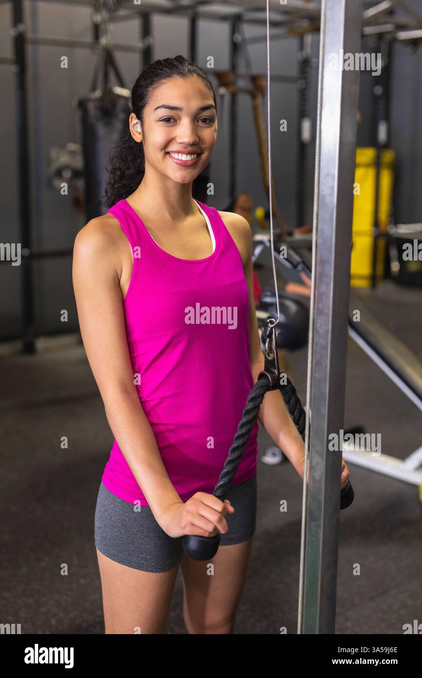 Donna in palestra che sorride mentre usa la macchina via cavo per allenarsi con la forza Foto Stock