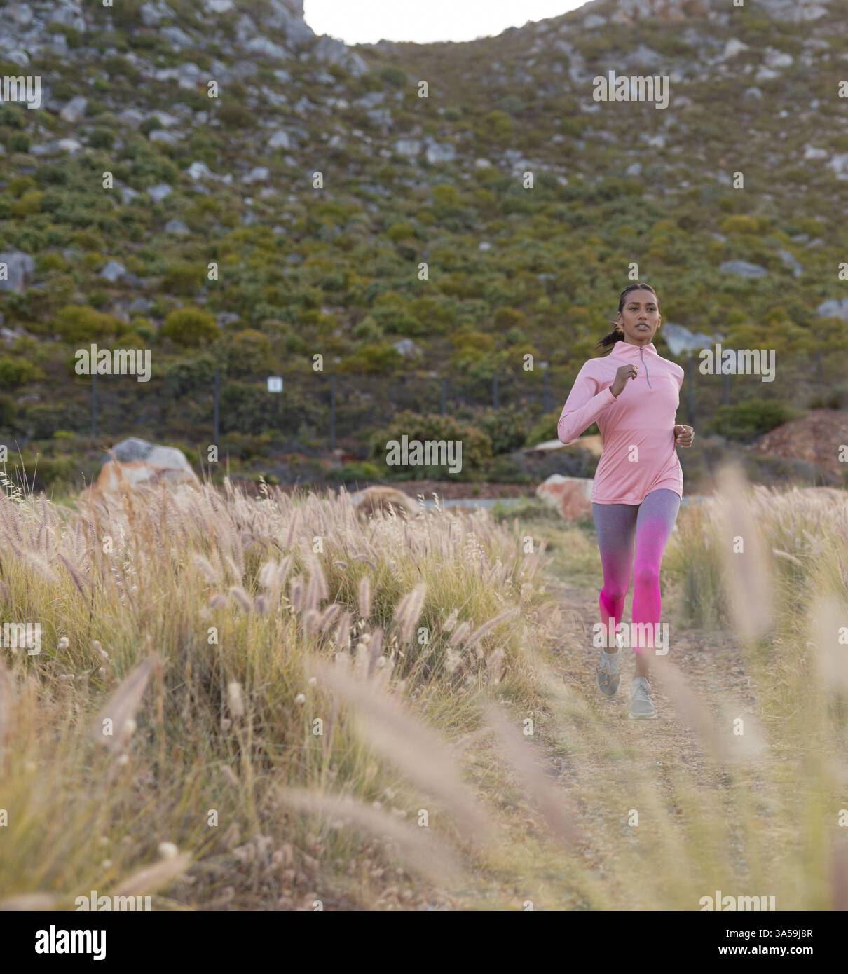 Donna che fa jogging sul sentiero attraverso il paesaggio panoramico, abbracciando un percorso fitness all'aperto, spazio fotocopie Foto Stock