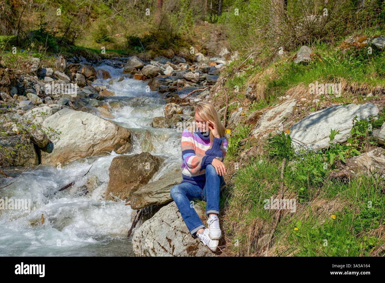 Una ragazza siede vicino a un fiume di montagna su rocce in una giornata di sole. Hinter-tux foto di alta qualità Foto Stock