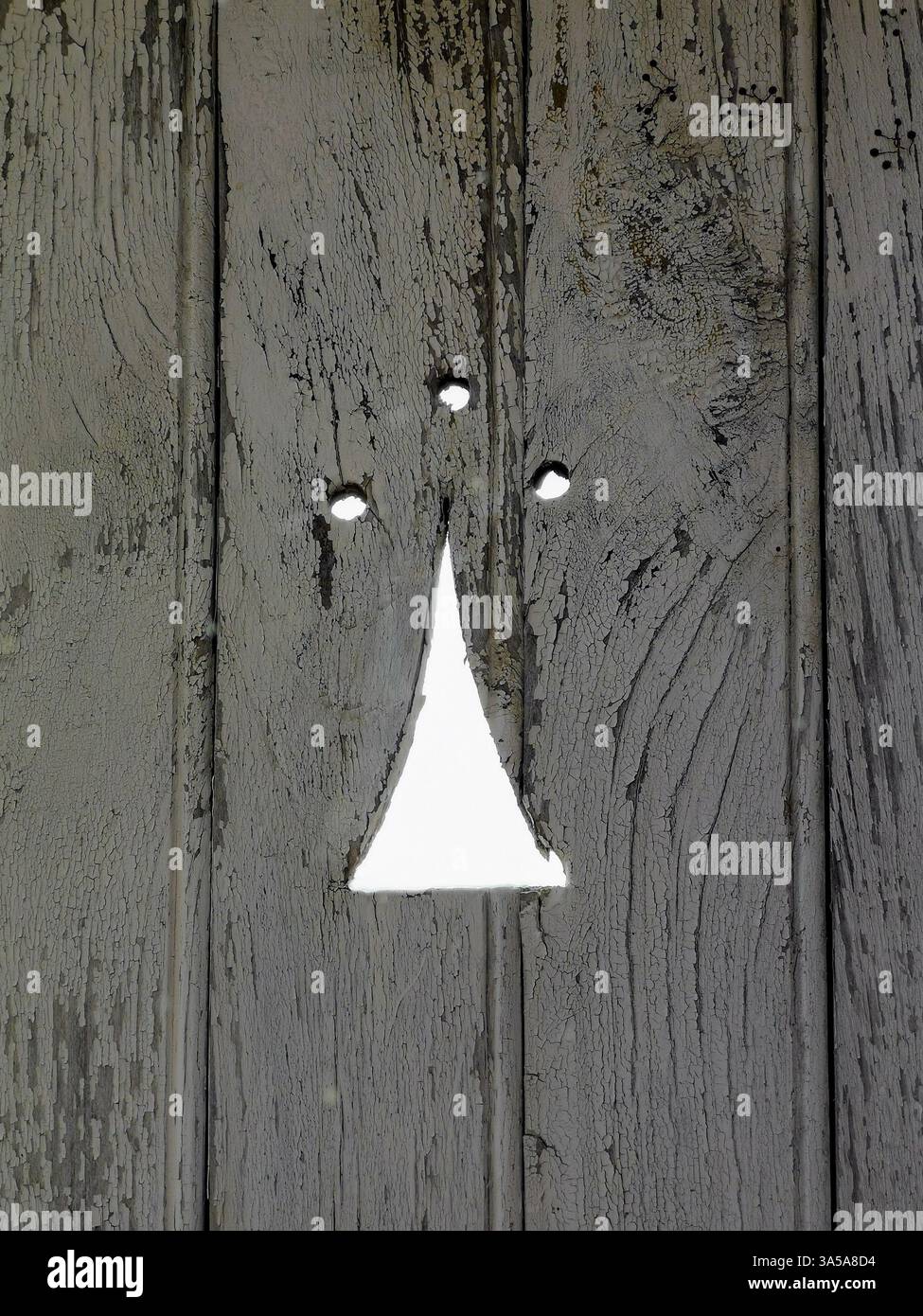 Una superficie in legno resistente agli agenti atmosferici presenta una fessura triangolare al centro, che consente alla luce di brillare. La consistenza del legno ne esalta l'arte Foto Stock