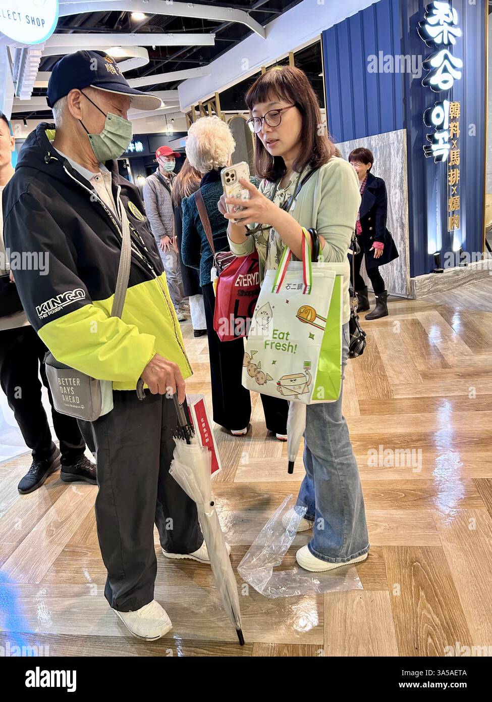 Taipei, Taiwan, affollano i taiwanesi, utilizzano smartphone all'interno di grandi magazzini, donna che parla con l'uomo, abbigliamento Taiwan - Immagine stock catturata con smartphone