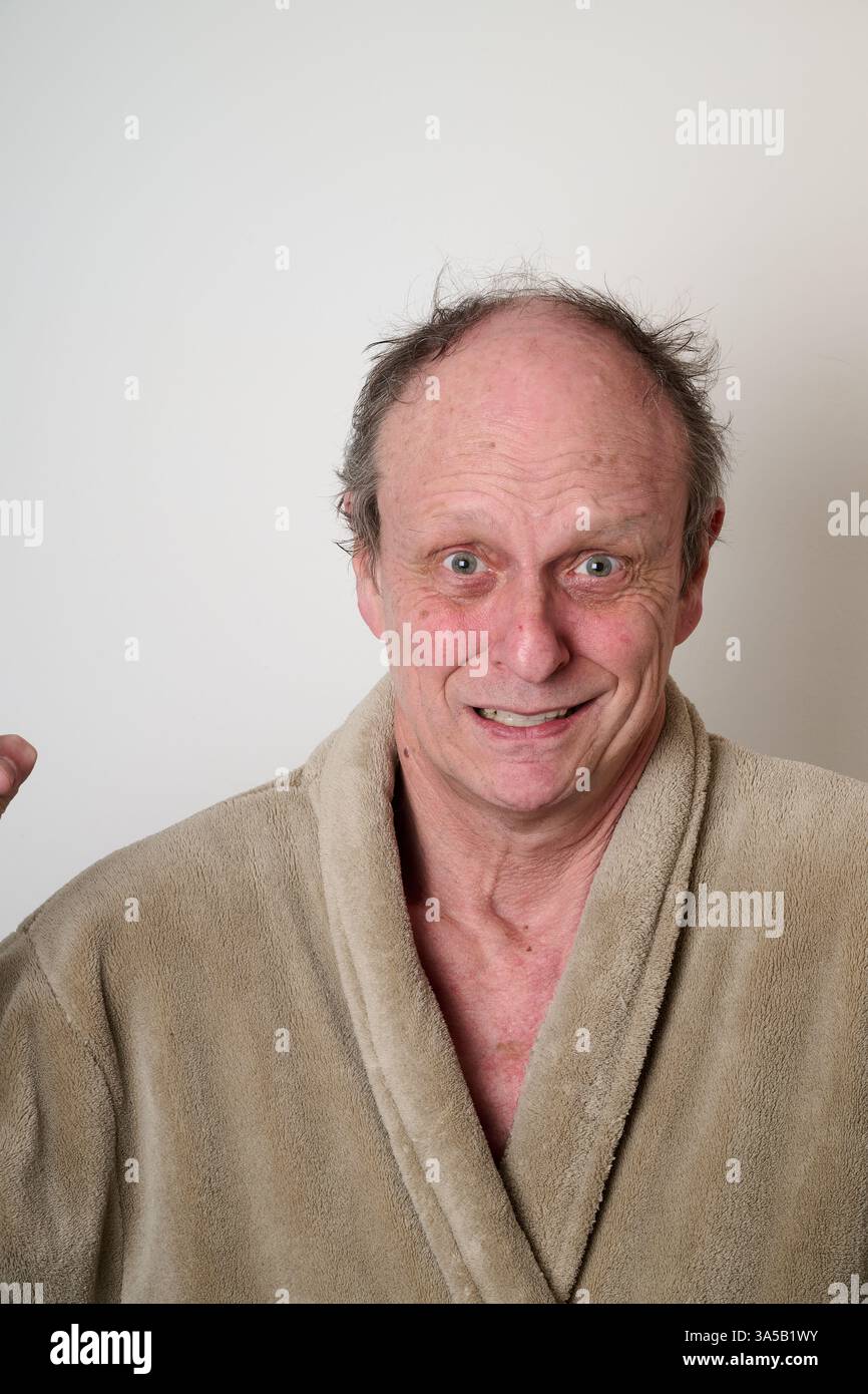 L'accappatoio beige di un vecchio uomo e i capelli duri fanno un brutto viso davanti alla fotocamera Foto Stock