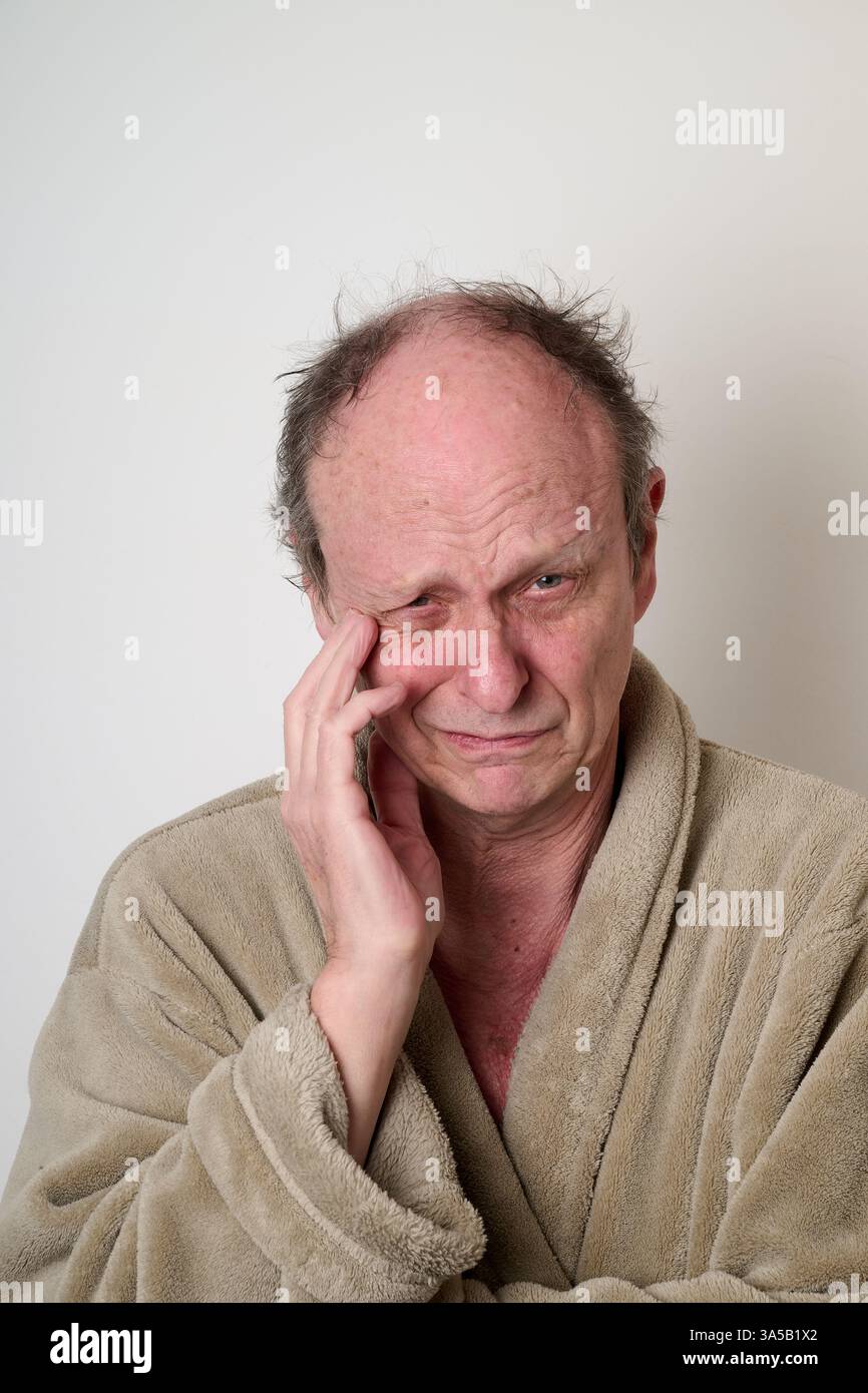 L'accappatoio beige di un vecchio uomo e i capelli duri fanno un brutto viso davanti alla fotocamera Foto Stock