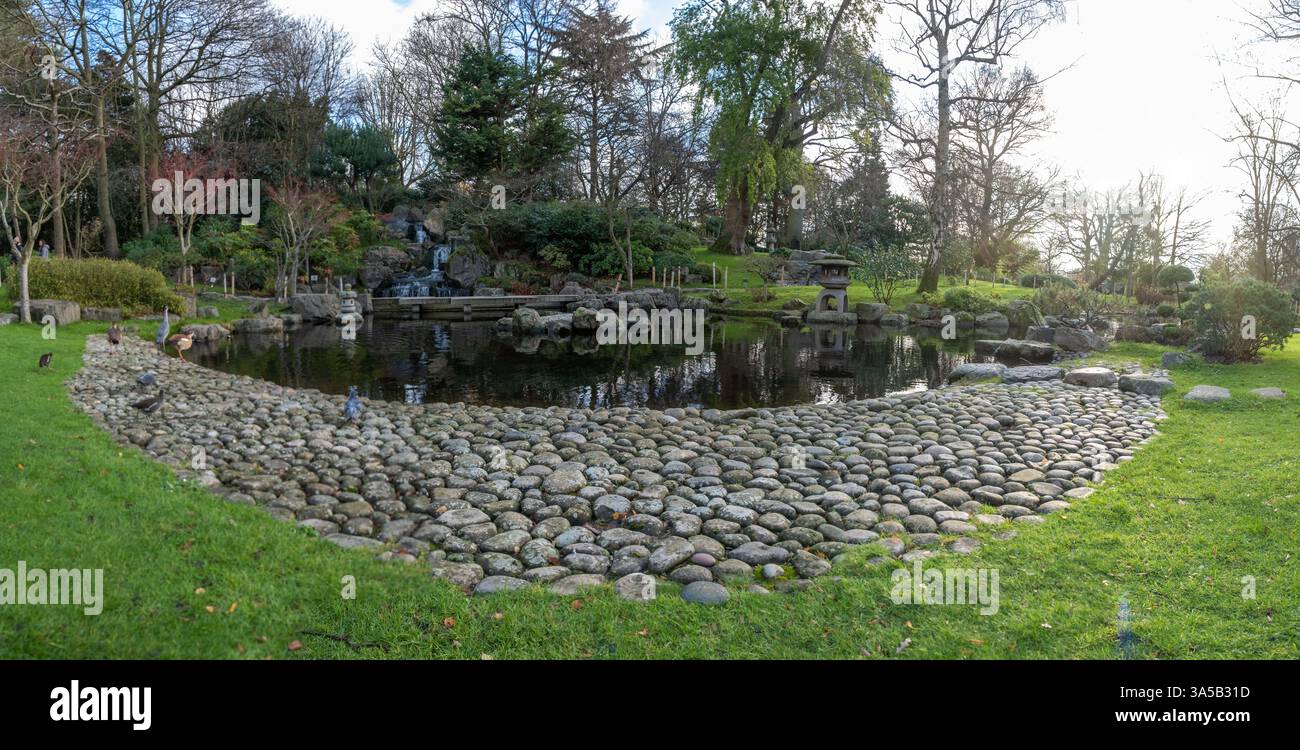 Sereno giardino giapponese in Holland Park, Londra, caratterizzato da un tranquillo laghetto, cascata, lussureggiante vegetazione e tradizionale lanterna in pietra. Tranquillo Foto Stock