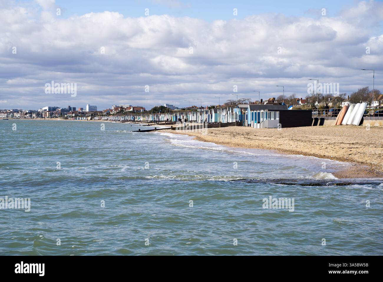 Vista di una fila di capanne costeggiate lungo la costa di Southend-on-SEA nella soleggiata giornata primaverile, onde d'acqua che si infrangono sulla spiaggia di ciottoli Essex Inghilterra Regno Unito Foto Stock