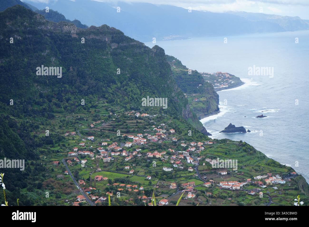 Pittoresco villaggio collinare affacciato sull'Oceano Atlantico sull'isola di Madeira, Portogallo, con lussureggianti montagne verdi e costa frastagliata Foto Stock