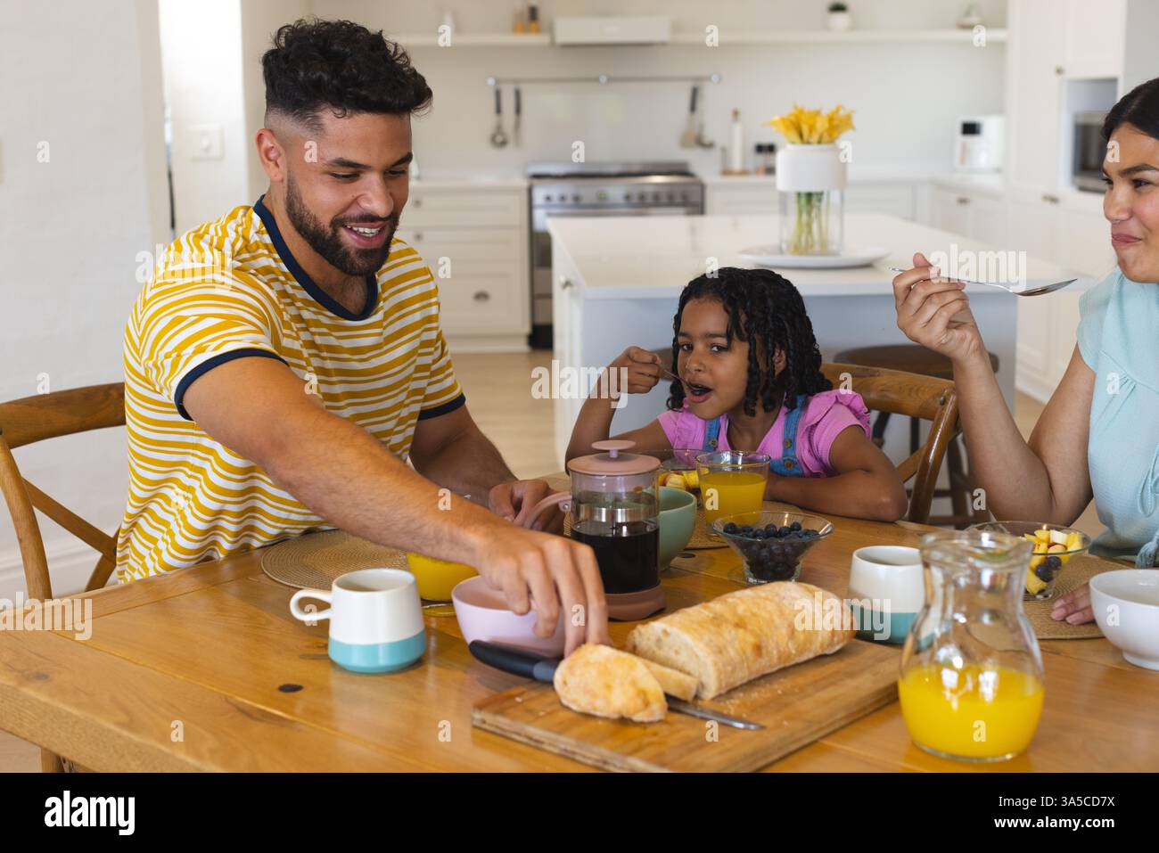 La famiglia gusta la colazione insieme a casa, sorridendo e condividendo il cibo intorno al tavolo Foto Stock
