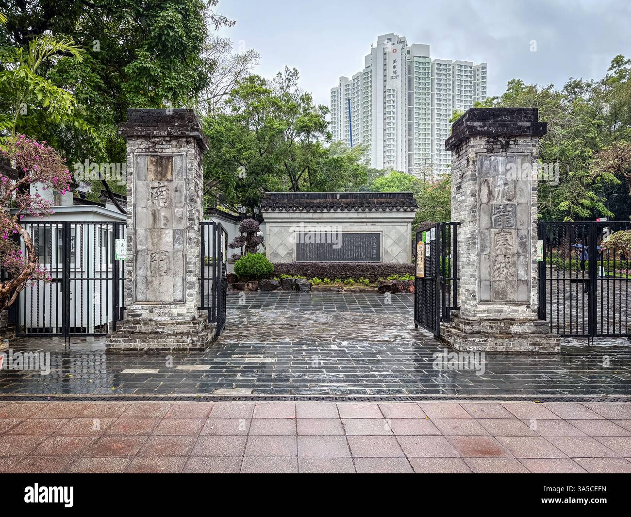 Porta d'ingresso al Parco cittadino murato di Kowloon, caratterizzato da tradizionali colonne di pietra, cancelli aperti e scorci dell'interno del parco di Hong Kong. Foto Stock