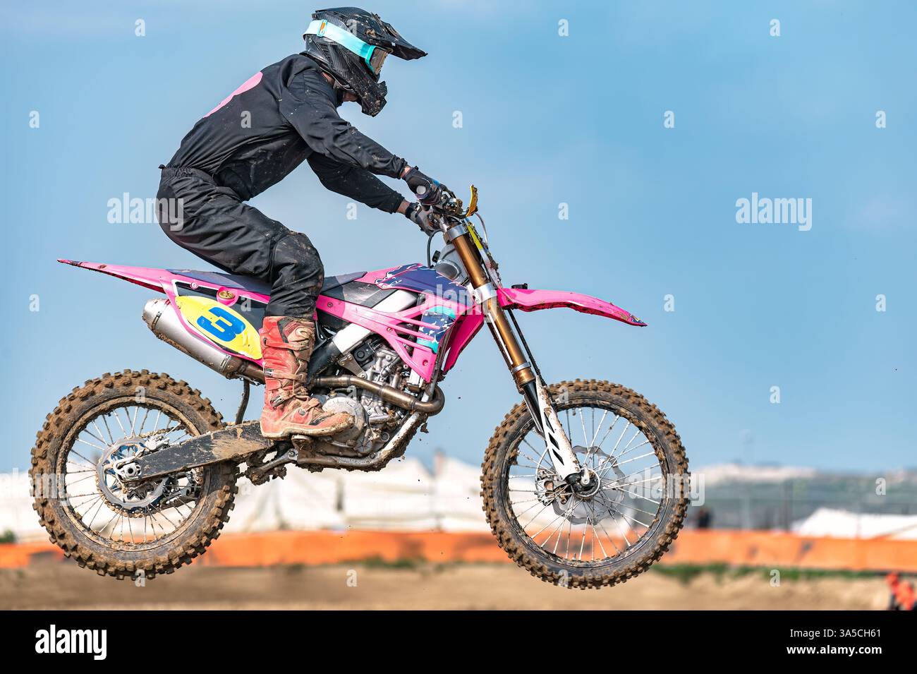 Il pilota di motocross sta volando in aria su una moto da terra rosa durante una gara, indossando l'equipaggiamento protettivo Foto Stock