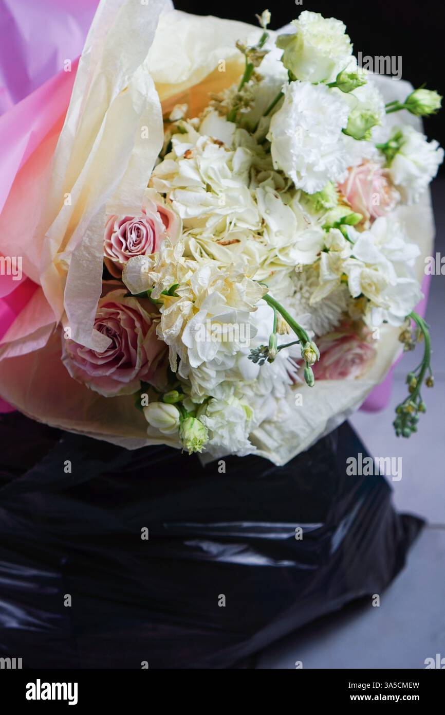 Un bouquet di fiori collocato all'interno di un sacchetto della spazzatura, che simboleggia l'amore perduto e la bellezza scartata. questa immagine rappresenta la fine di una relazione, dove i fiori, un tempo vibranti e pieni di vita, incarnano ora lo spreco emotivo di un legame rotto. incoraggia la riflessione sulla natura fugace dell'amore, mentre aumenta la consapevolezza sui rifiuti e sulle questioni ambientali. Foto Stock