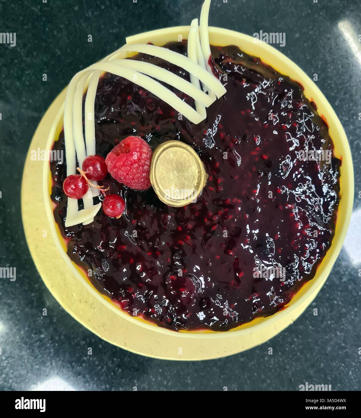 Una crostata di mirtilli splendidamente lavorata presenta una crema di frutti di bosco lucida e decorazioni di lamponi e cioccolato bianco, che mostrano l'esperienza nel settore della panificazione. Foto Stock