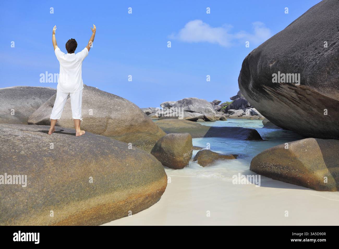 Thailandia. Splendida spiaggia sulle Isole Similan. Donna di mezza età vestita di bianco che fa yoga. Pose la Benedizione del Sole Foto Stock
