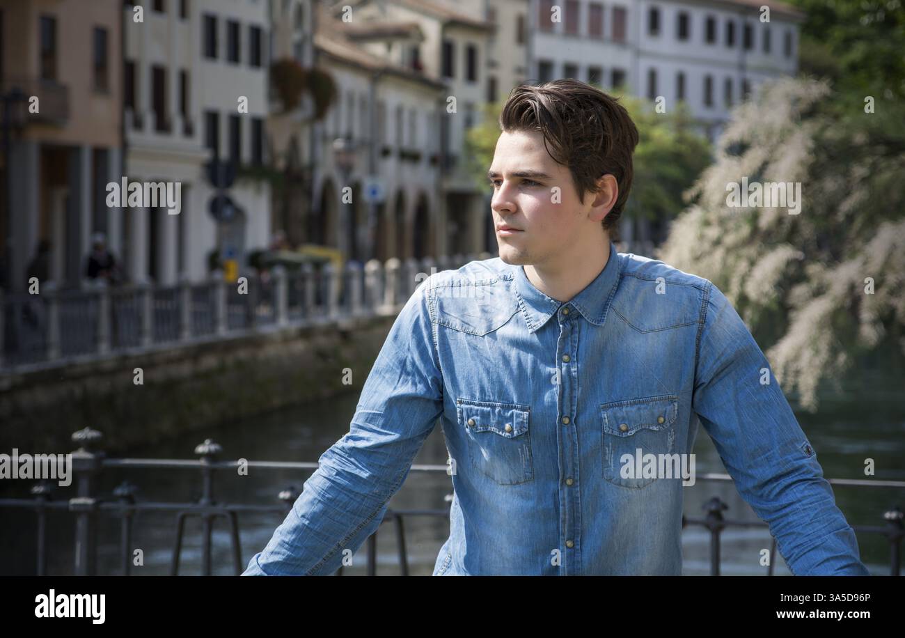 Giovane uomo che indossa una camicia in denim sul ponte cittadino di Treviso, Italia, Europa Foto Stock