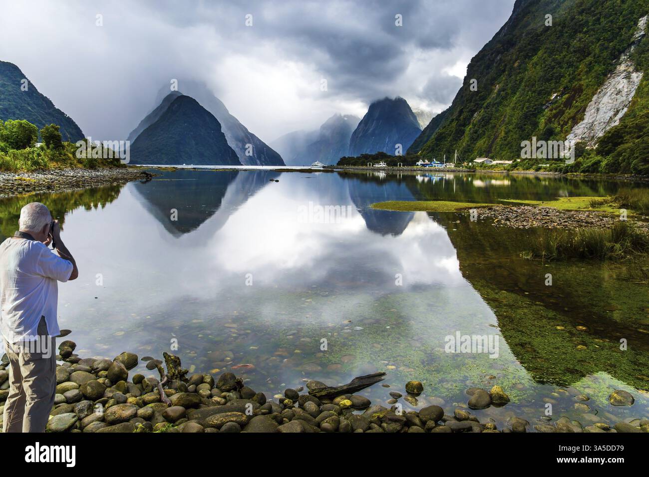 Nuova Zelanda. Il fiordo dell'oceano Milford Sound. I turisti dai capelli grigi fotografano un paesaggio. L'acqua fiorita a specchio riflette le montagne. Concetto di Foto Stock