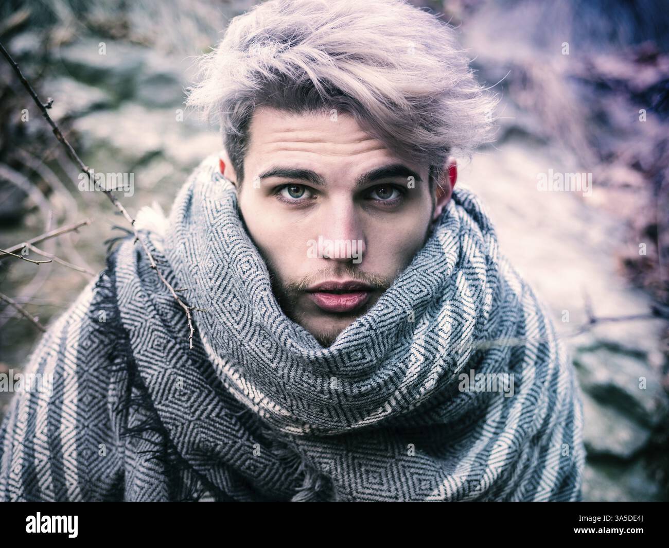 Colpo di testa di un giovane uomo con cappuccio che posa all'aperto in inverno con la neve intorno, guardando la fotocamera Foto Stock
