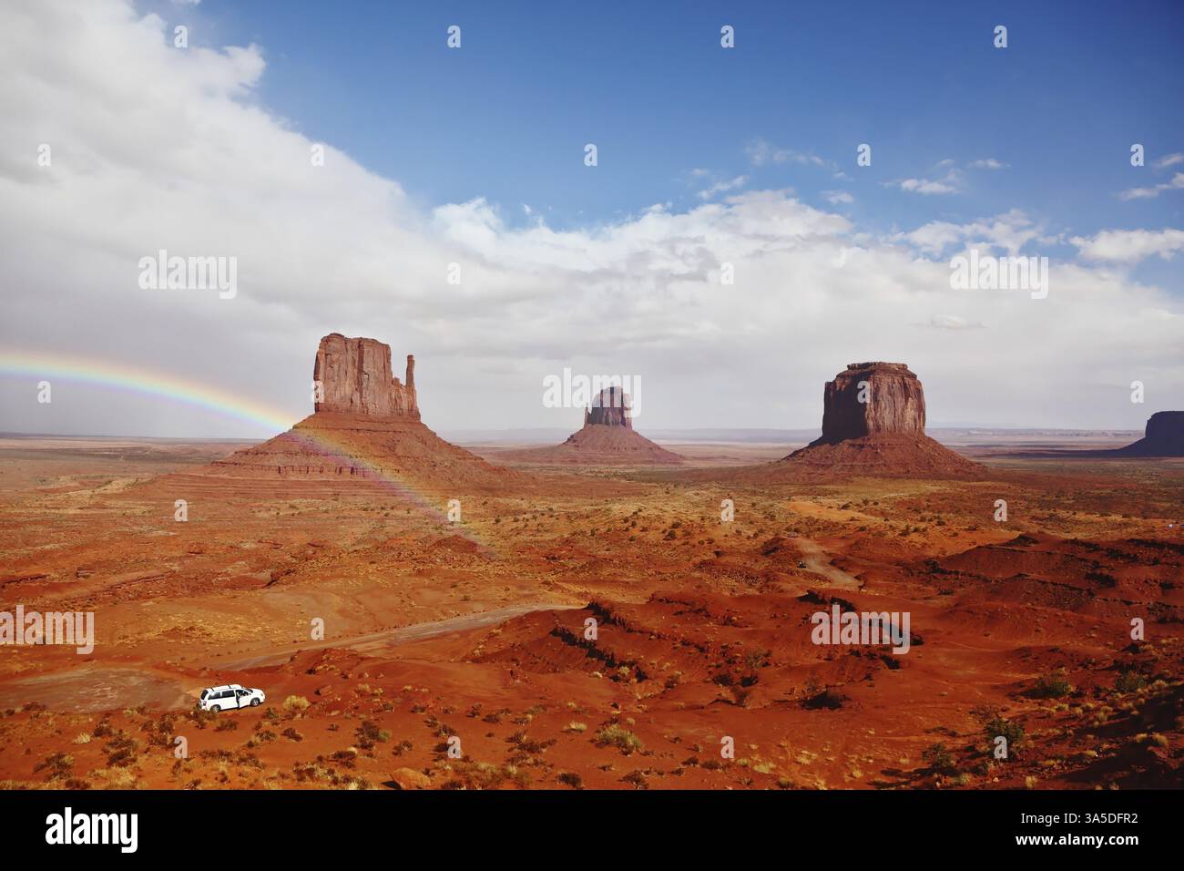 Deserto di pietra rossa Navajo, Stati Uniti. Rocce isolate - i guanti si intersecano con il bellissimo arcobaleno. Sulla strada c'è una jeep bianca Foto Stock