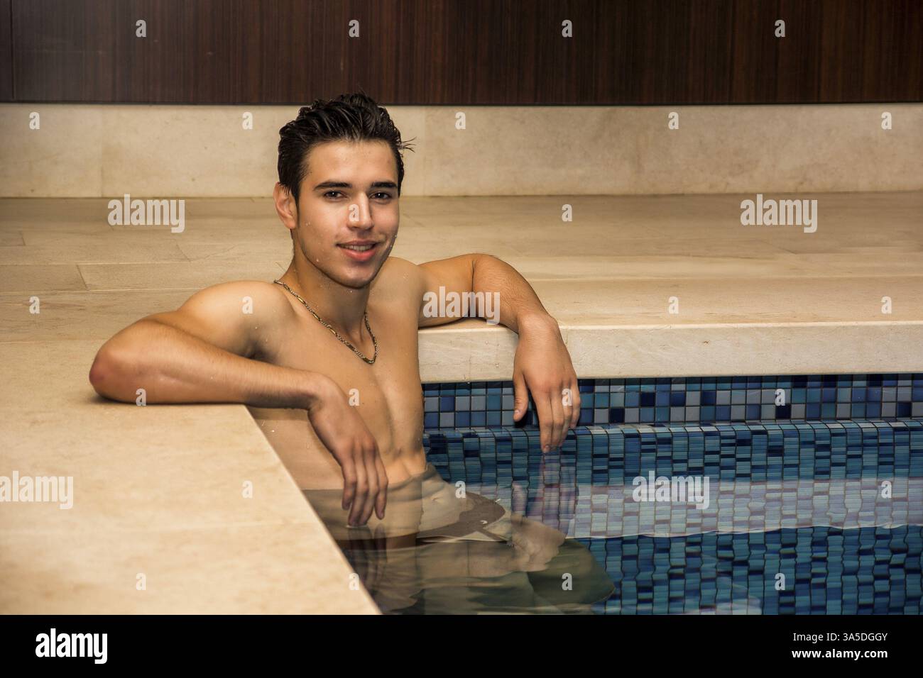 Giovane uomo appeso sul bordo piscina rilassante in un ambiente tranquillo Foto Stock
