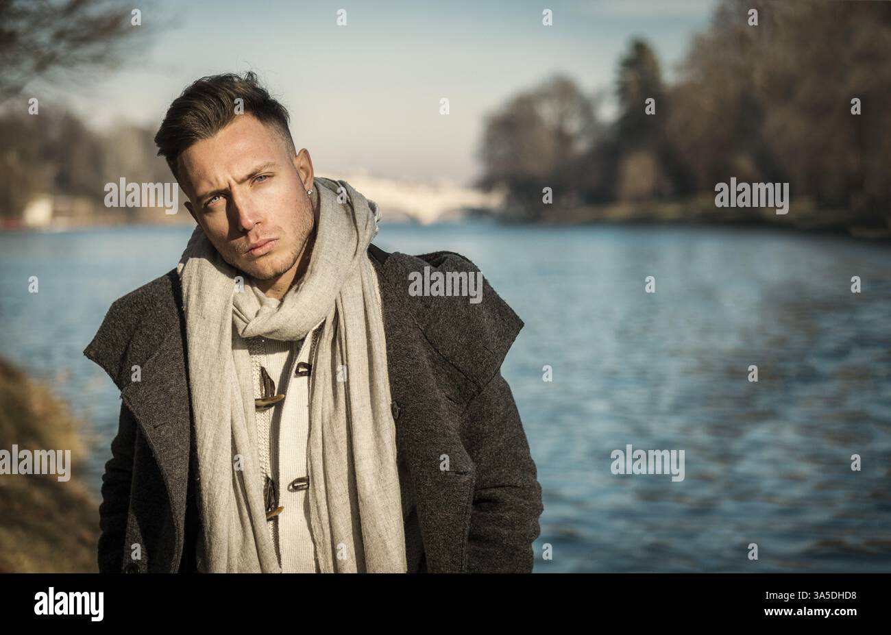 Un bel giovane in ambientazione urbana nella città europea, Torino in Italia, vicino al po, nelle fredde giornate invernali, che guarda la macchina fotografica Foto Stock