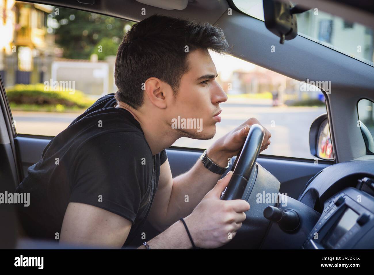 Profilo di un giovane che guida la vettura e si inclina in avanti e sbircia attraverso il parabrezza dell'auto Foto Stock