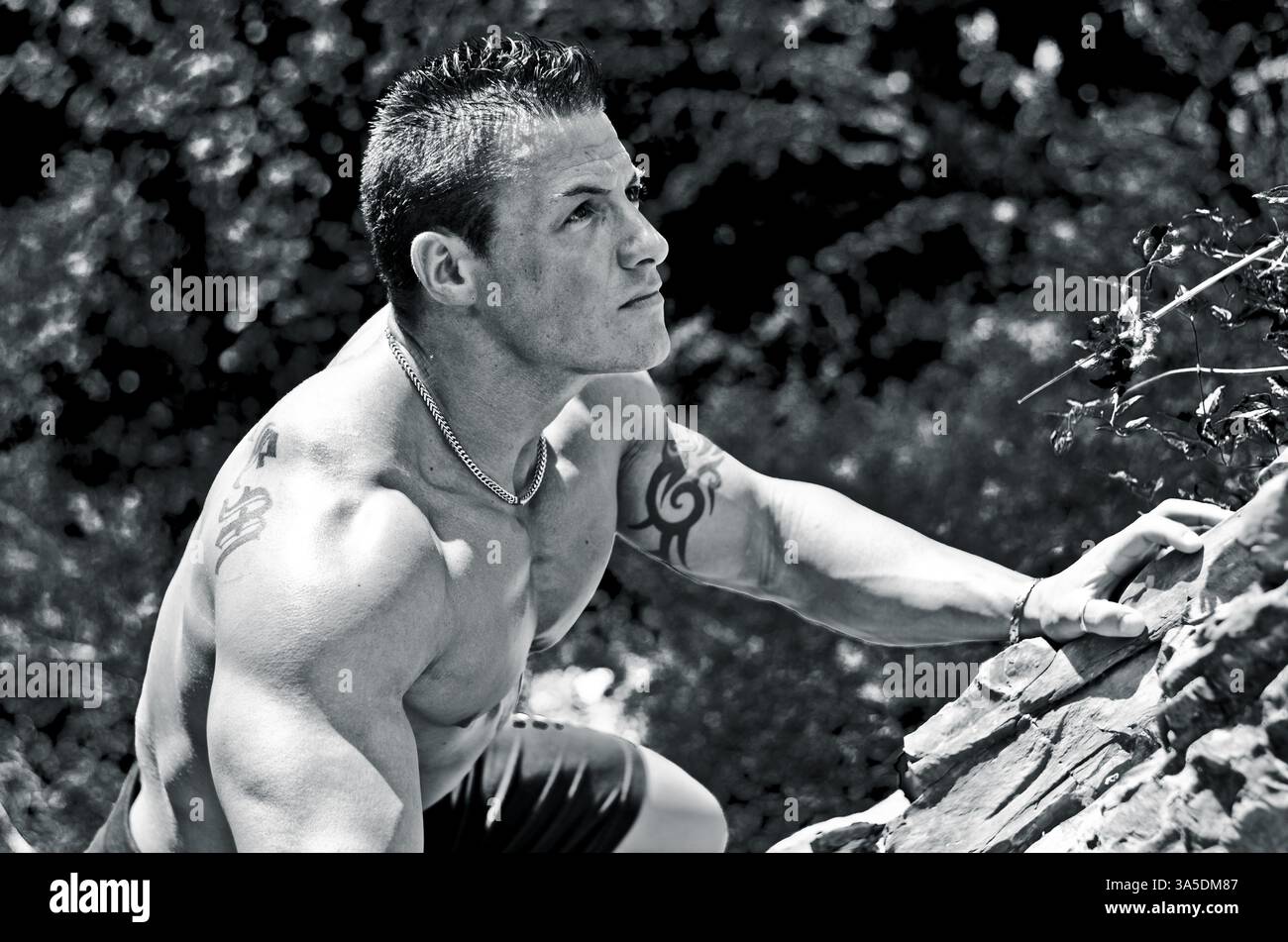 Bello, muscolare, shirless scalatore, cercando nella fotocamera e arrampicata parete di pietra Foto Stock