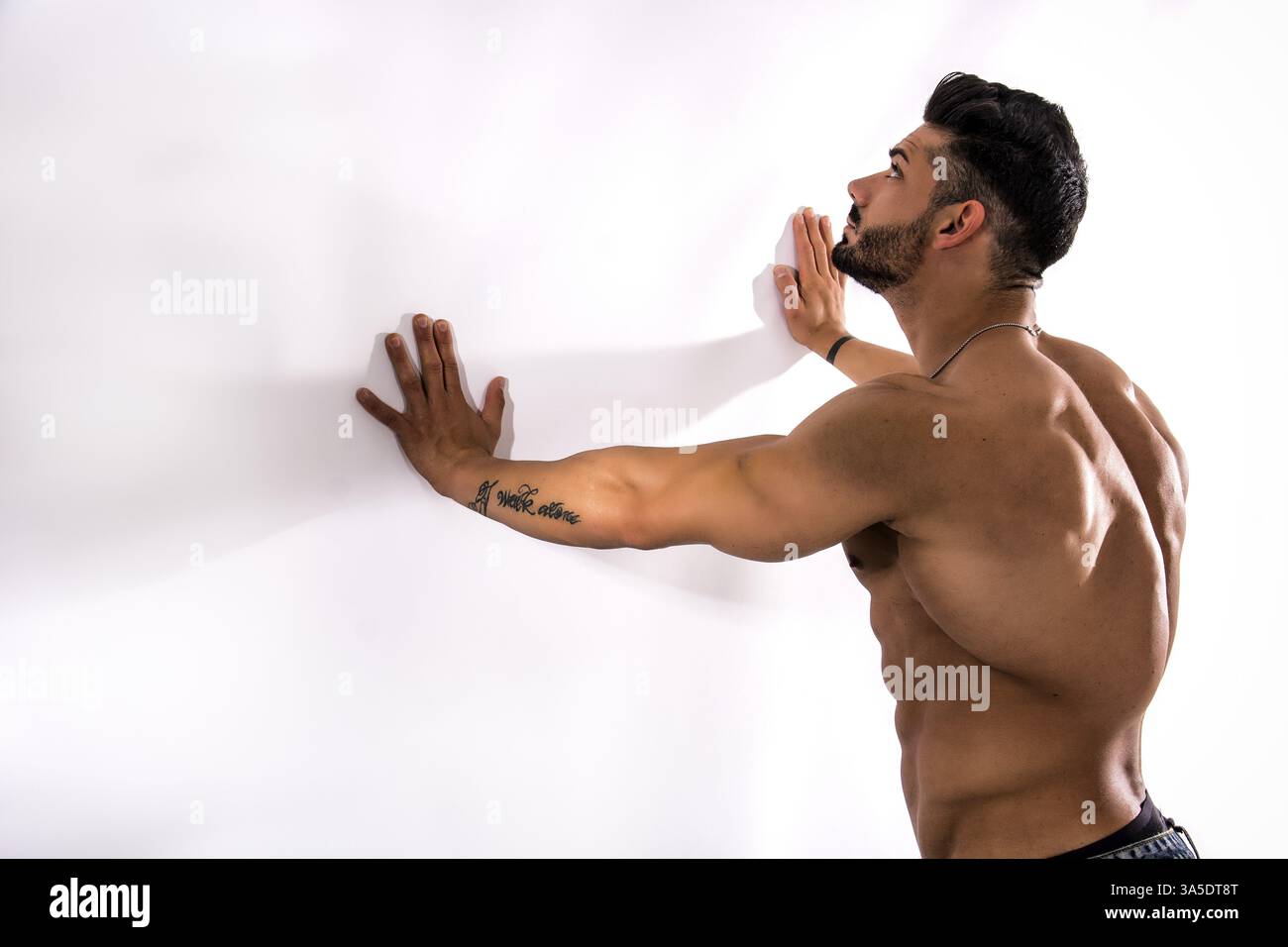 Culturista muscoloso appoggiato contro la parete bianca, guardandolo, con un ampio spazio imitabile accanto a lui Foto Stock