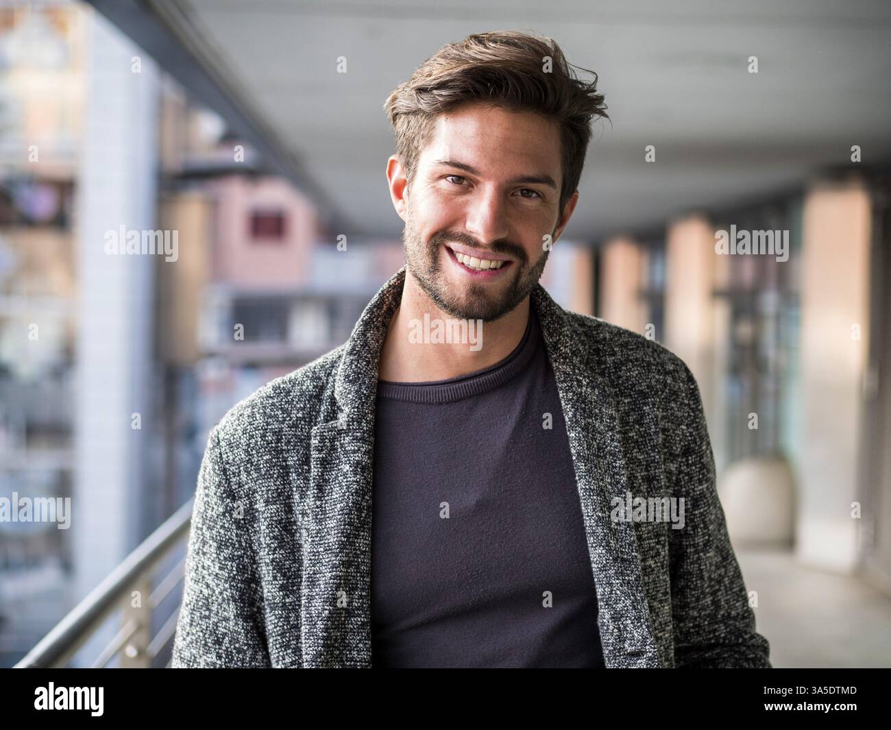 Un bel giovane in un ambiente urbano in una città europea, in piedi e sorridente alla macchina fotografica felice Foto Stock