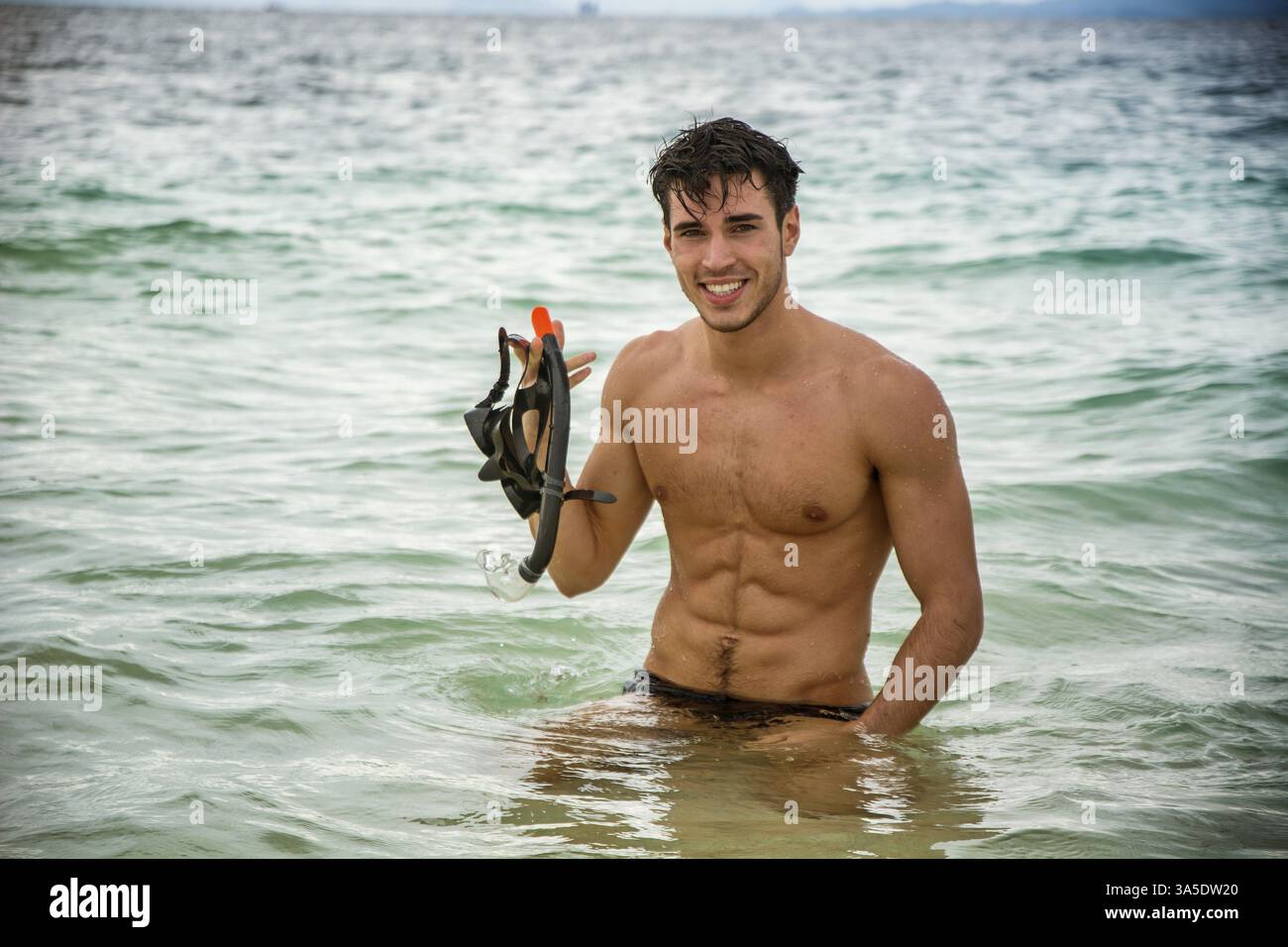 Giovane uomo muscoloso e bello in pantaloni da nuoto che tiene la maschera da immersione e guarda la macchina fotografica Foto Stock