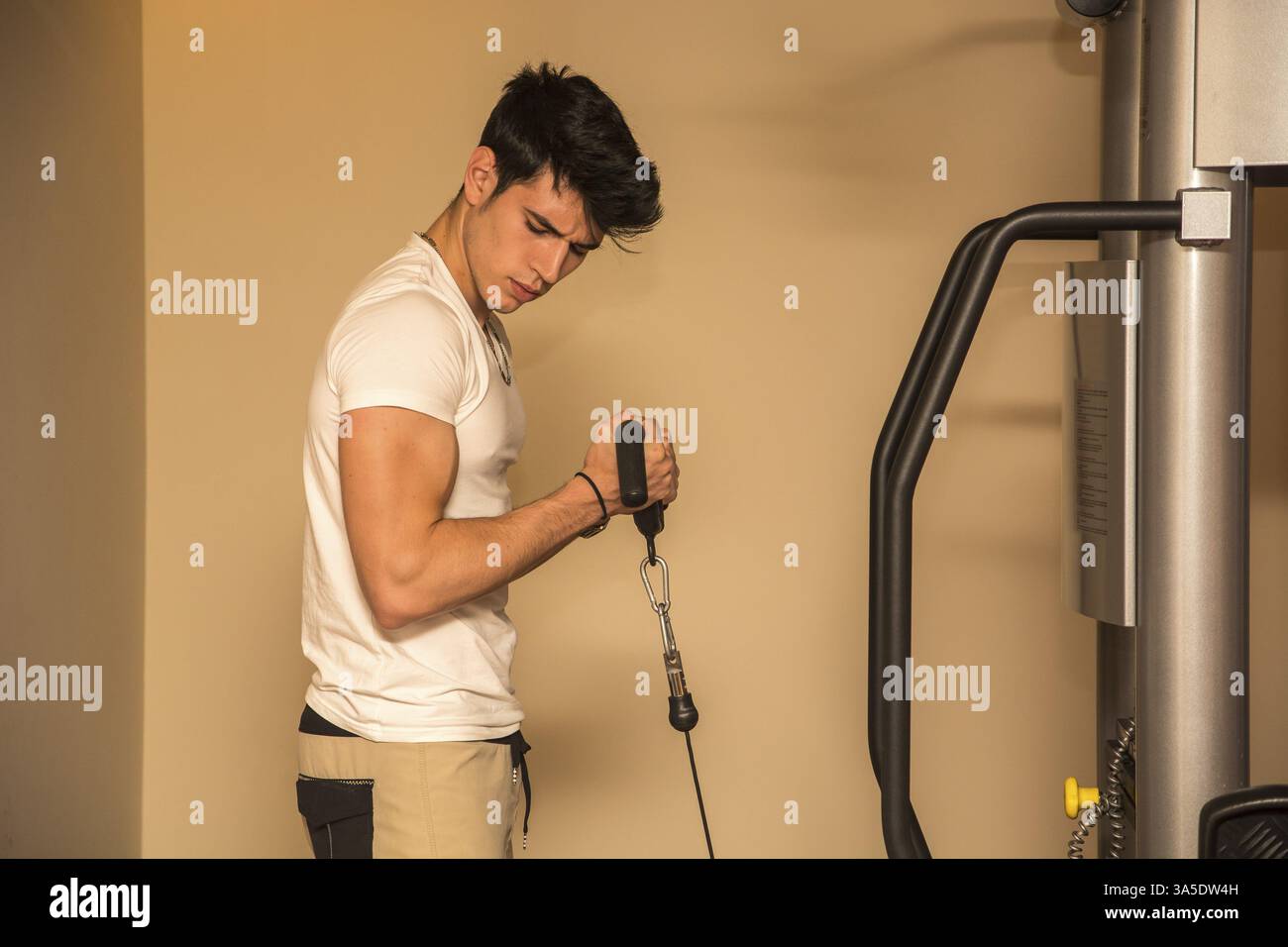 Bel giovane esercizio bicipite sulle attrezzature da palestra, tiro da sotto Foto Stock