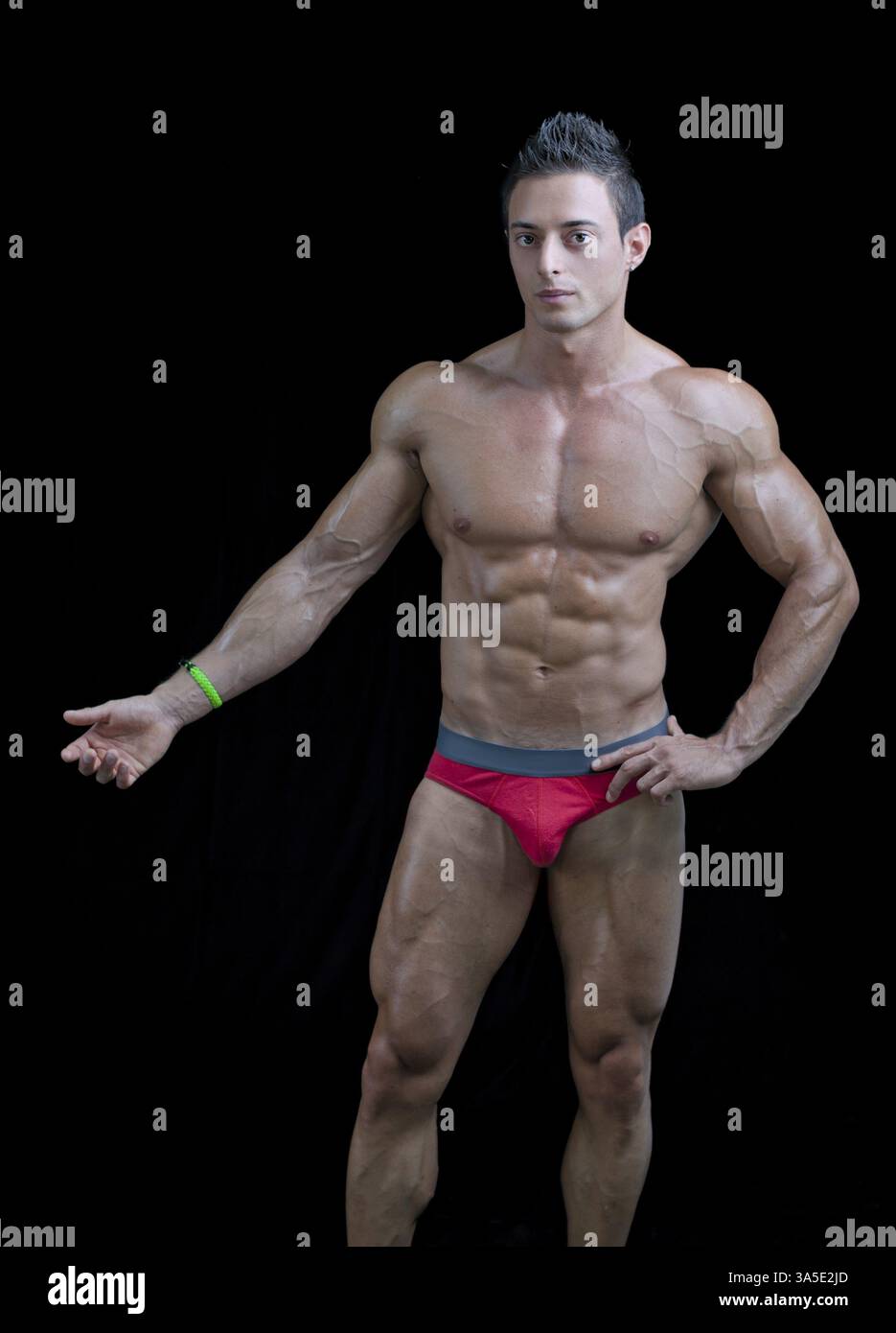 Giovane culturista muscoloso in posa rilassata, una mano mostra qualcosa. Isolato sul nero Foto Stock