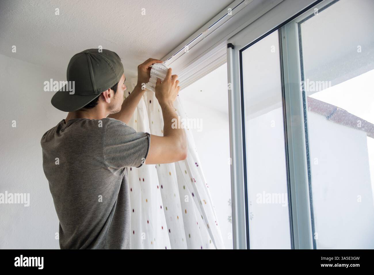 Giovane uomo bello o tuttofare installazione tende alle finestre di casa, facendo lavori di rinnovo Foto Stock