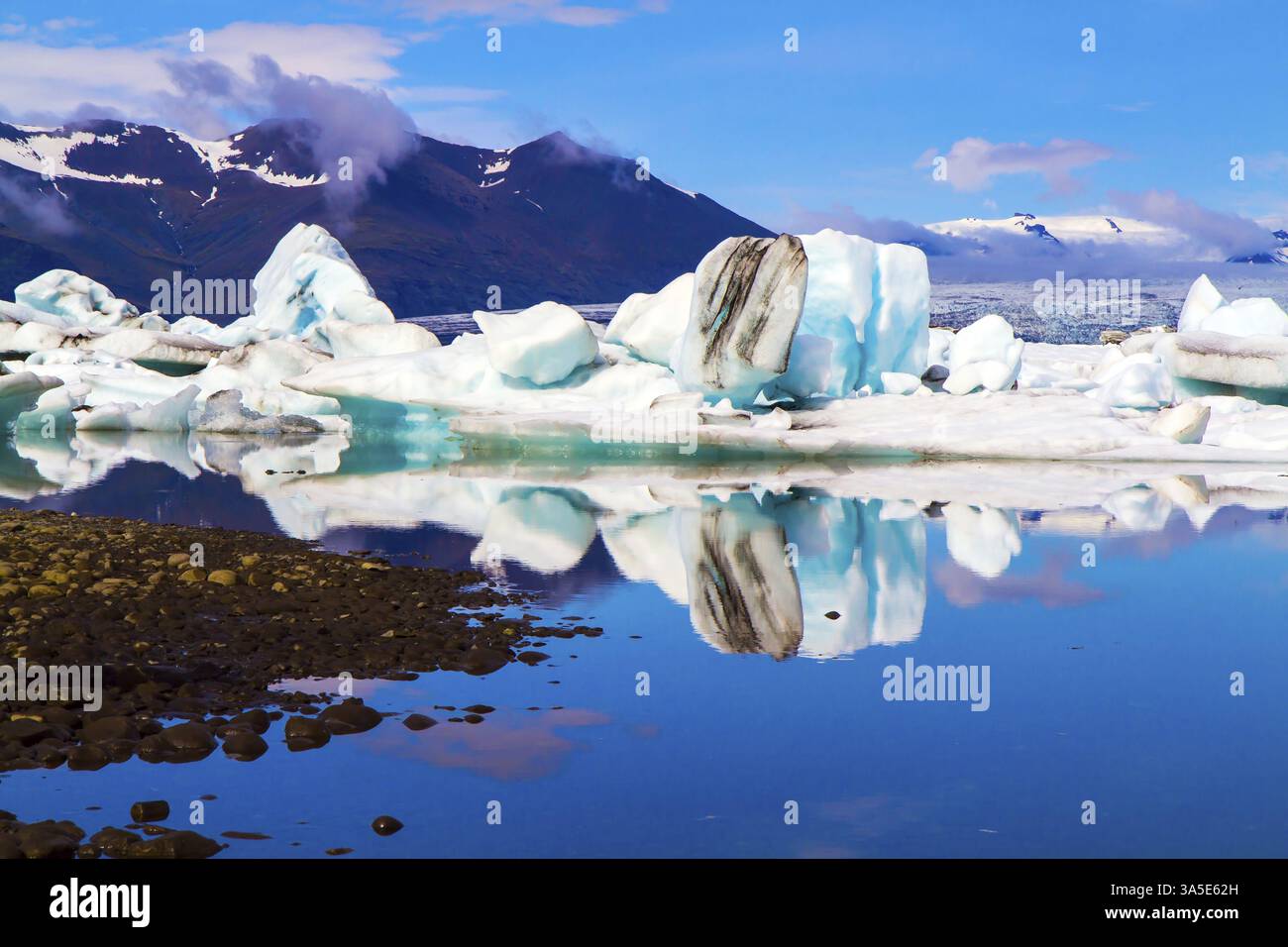 Iceberg bianchi e blu e banchi di ghiaccio riflessi nell'acqua. Islanda. La laguna di Jokulsaurloun. Il ghiaccio è coperto di cenere vulcanica. Il concetto di no Foto Stock