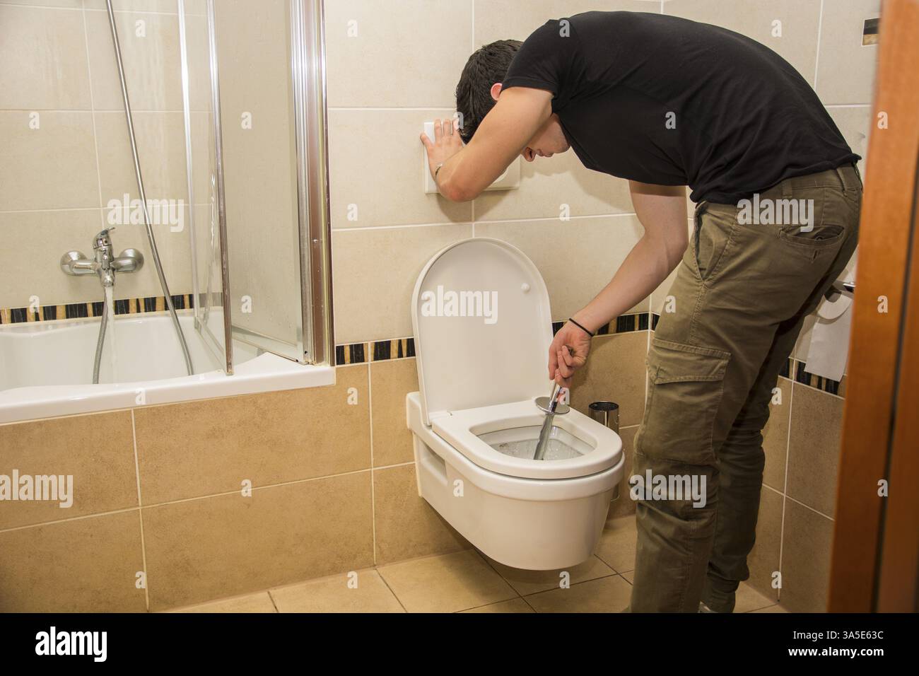 Bel giovane la piegatura verso il basso con una spazzola in mano la pulizia del bagno wc, strofinando la latrina in ceramica Foto Stock