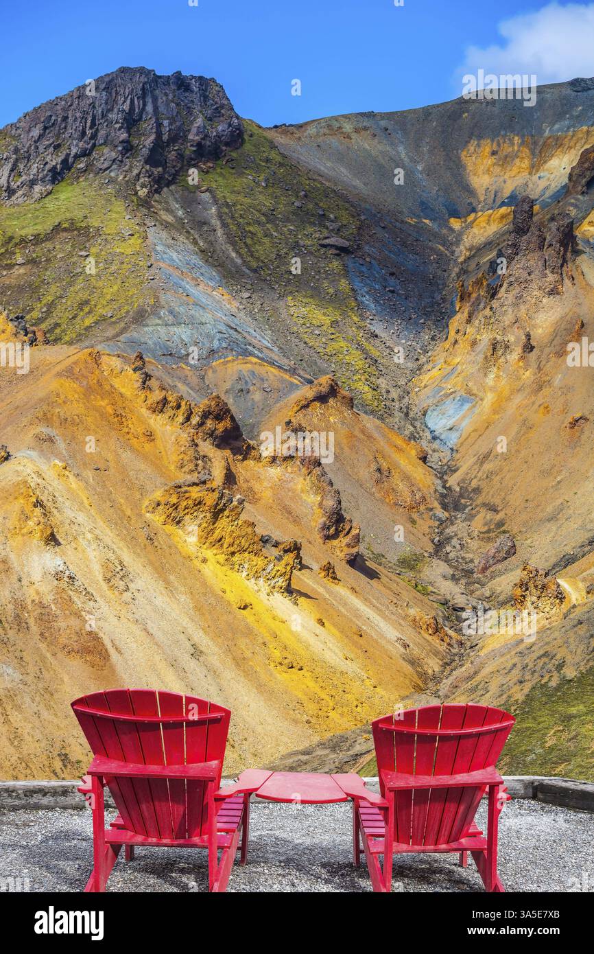 Montagne multicolore di riolite minerale sono illuminate dal sole. Due chaise longue rosse collegate da un piccolo tavolo per i turisti Foto Stock